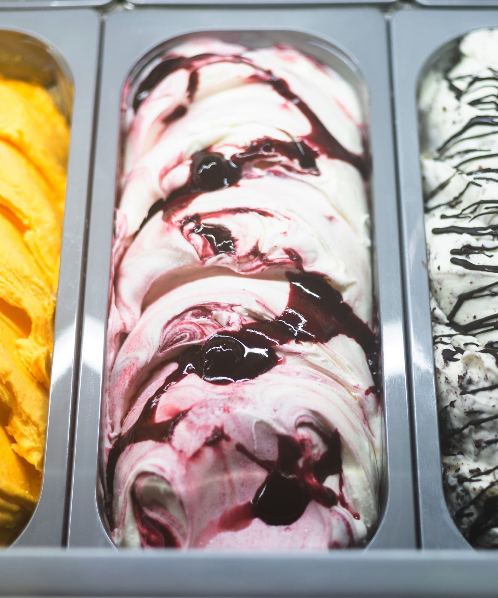 Gelato display with mango, cherry swirl, and cookies & cream flavors.