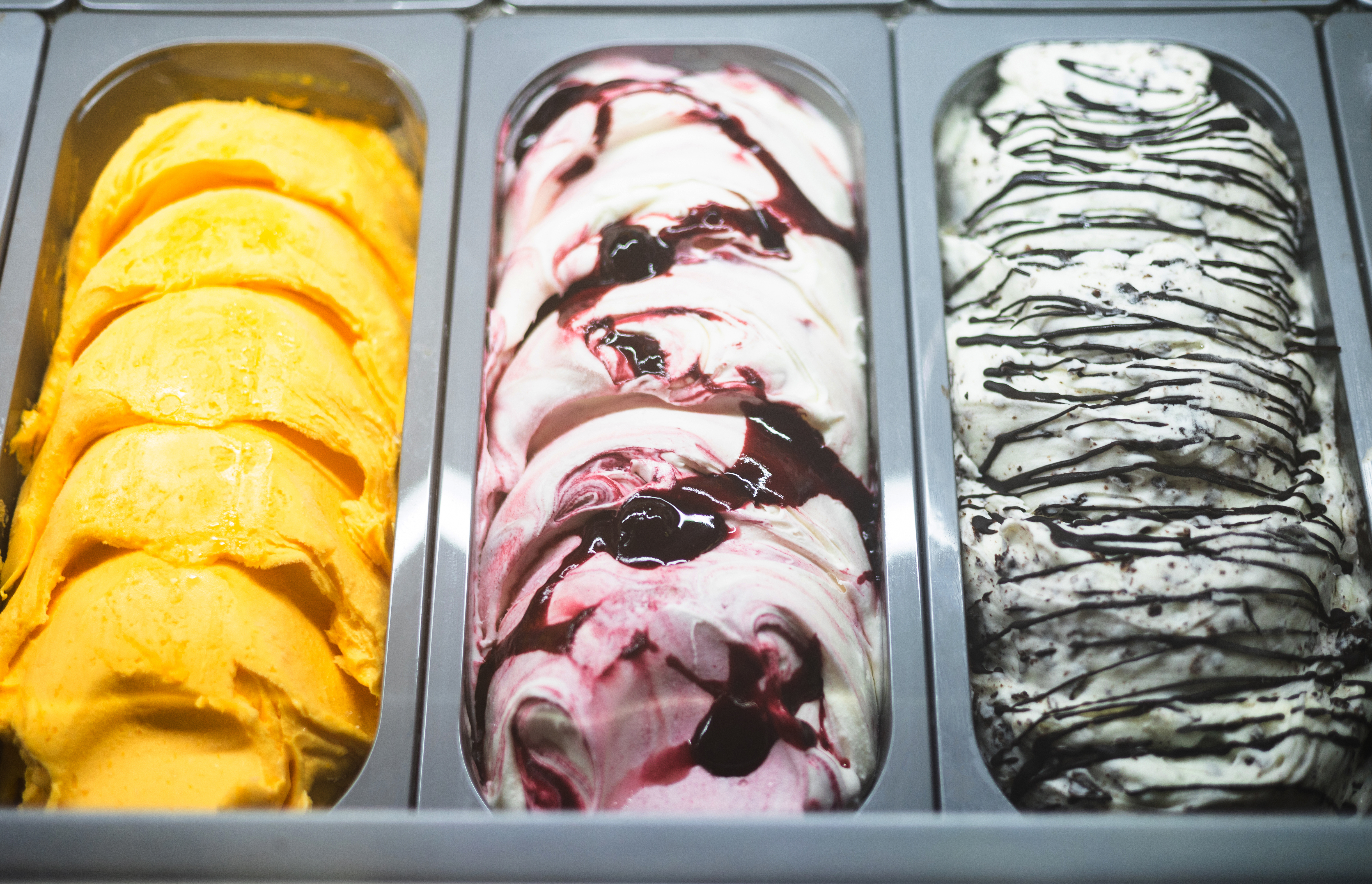Gelato display with mango, cherry swirl, and cookies & cream flavors.