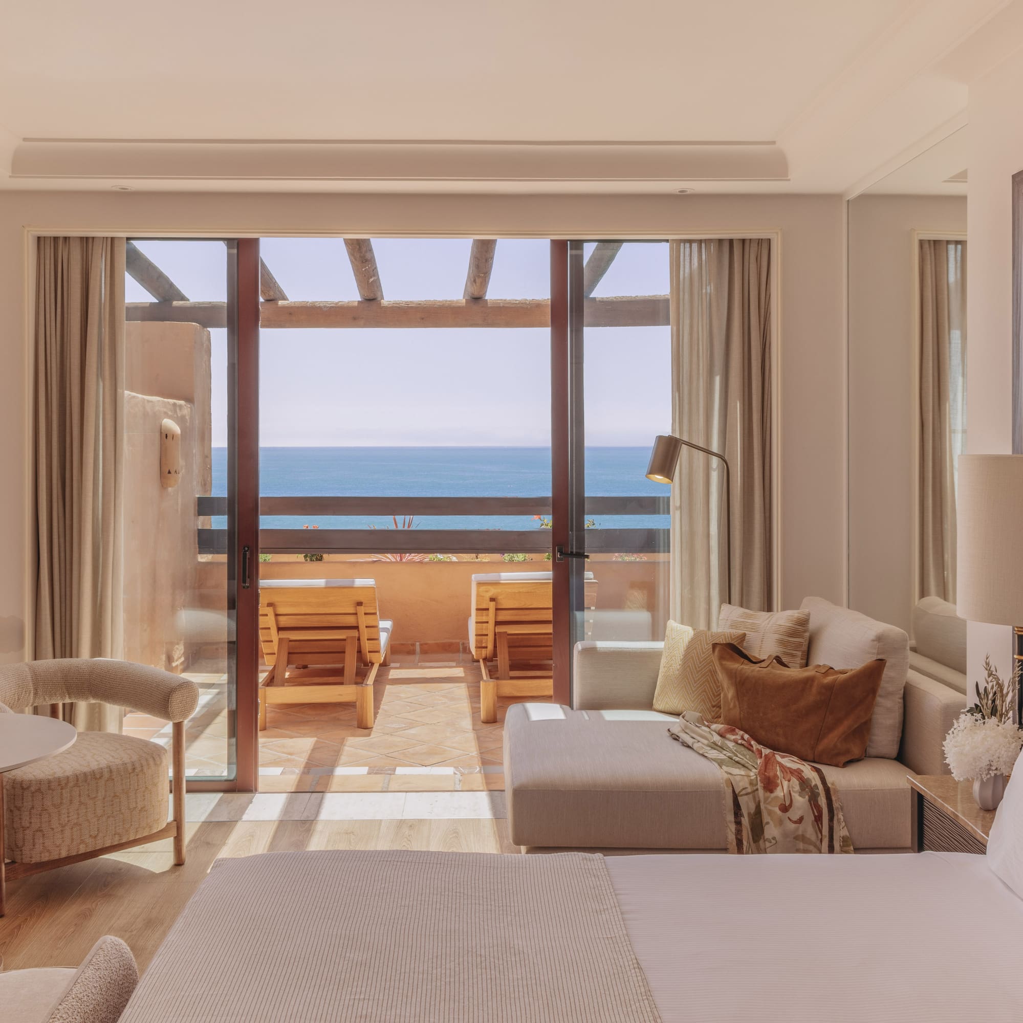 Ocean view hotel room with balcony, outdoor lounge chairs, bed, and sofa.