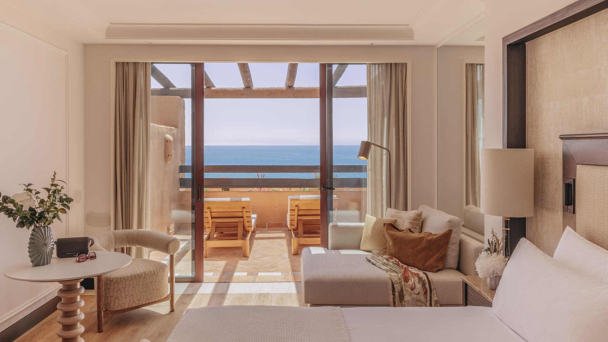 Ocean view hotel room with balcony, outdoor lounge chairs, bed, and sofa.