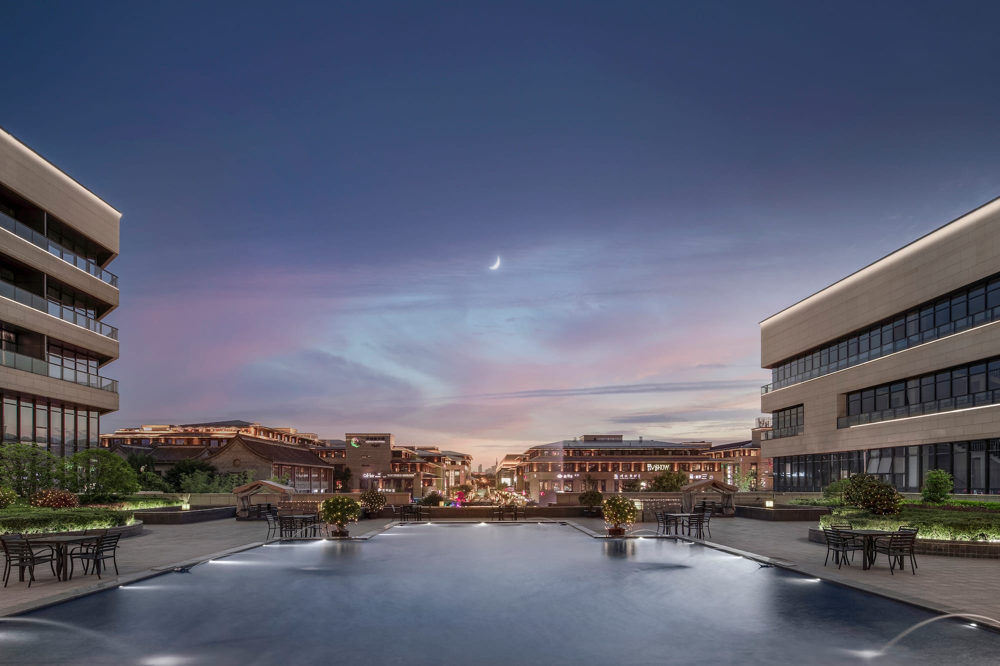 Twilight plaza with modern buildings, reflecting pool, and crescent moon.