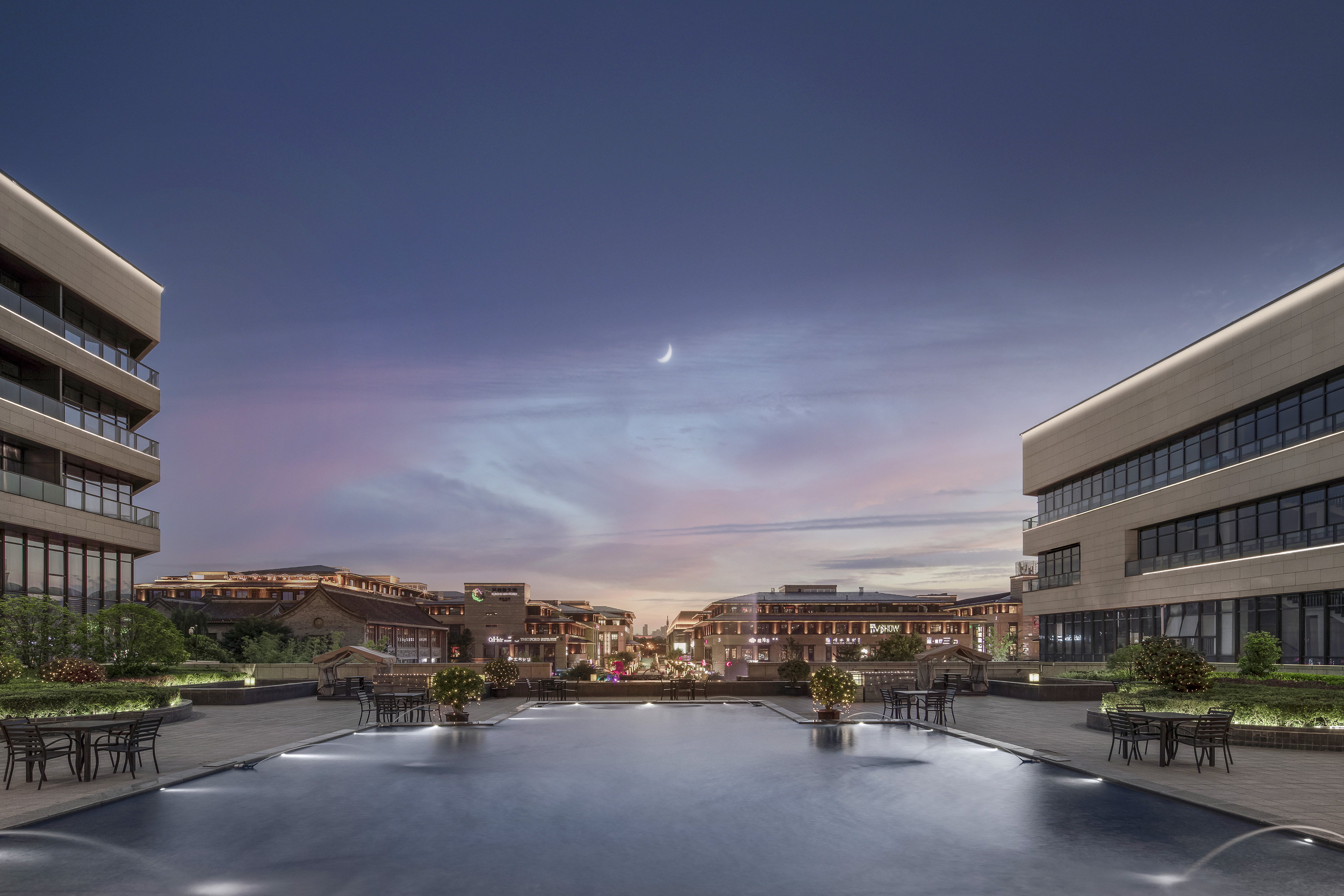 Twilight plaza with modern buildings, reflecting pool, and crescent moon.
