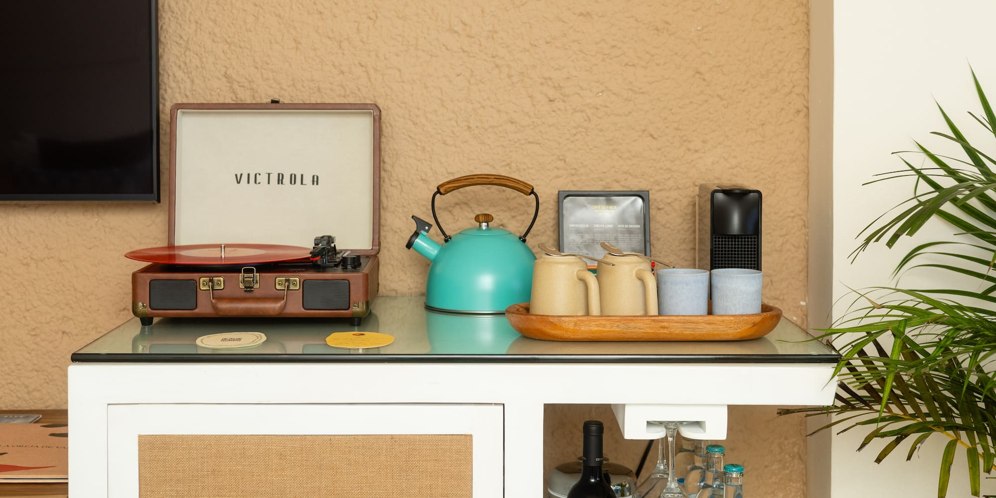 Tocadiscos Victrola, tetera turquesa y minibar en habitación de hotel.