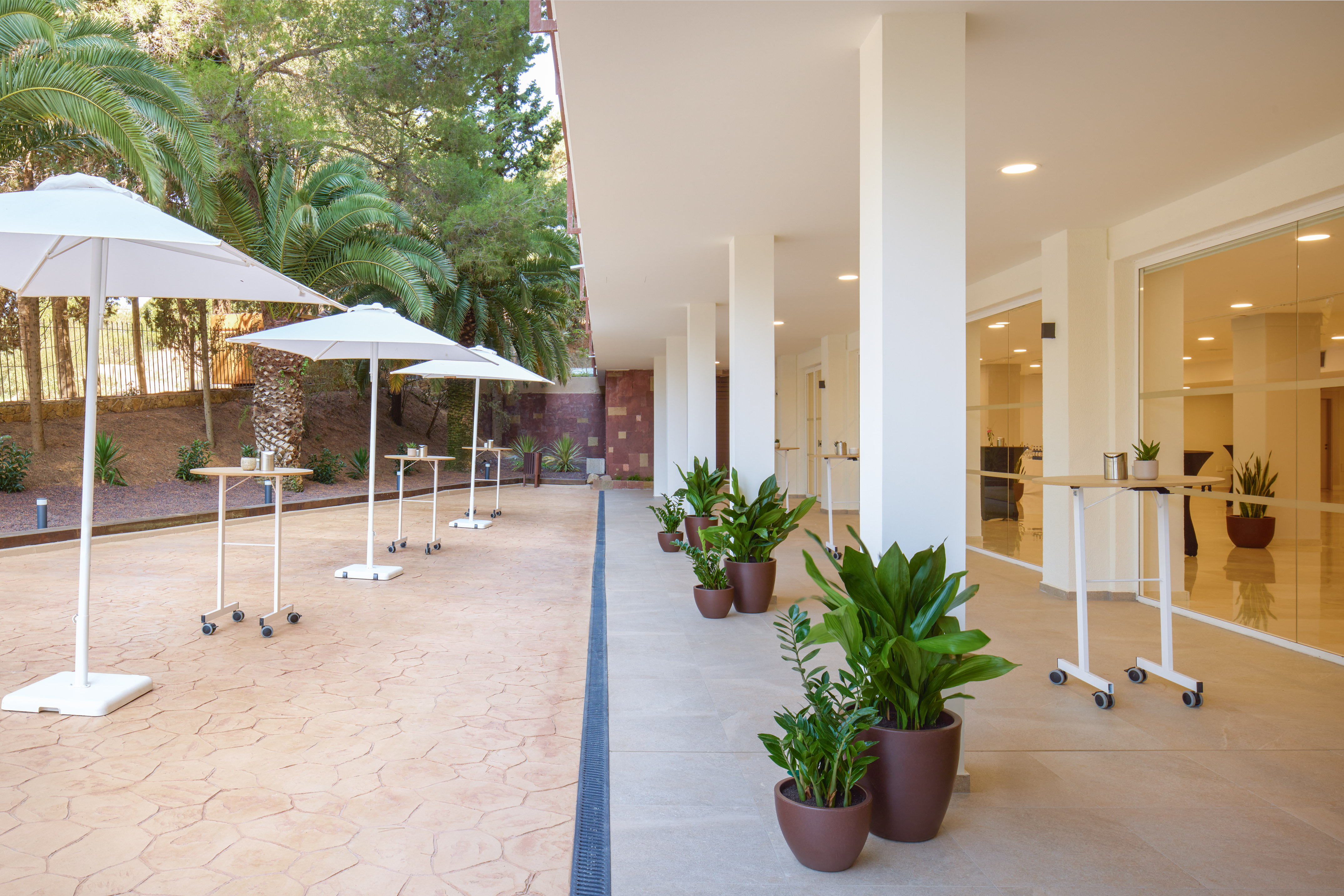 Modern outdoor patio for events with umbrellas, high tables, and palm trees.