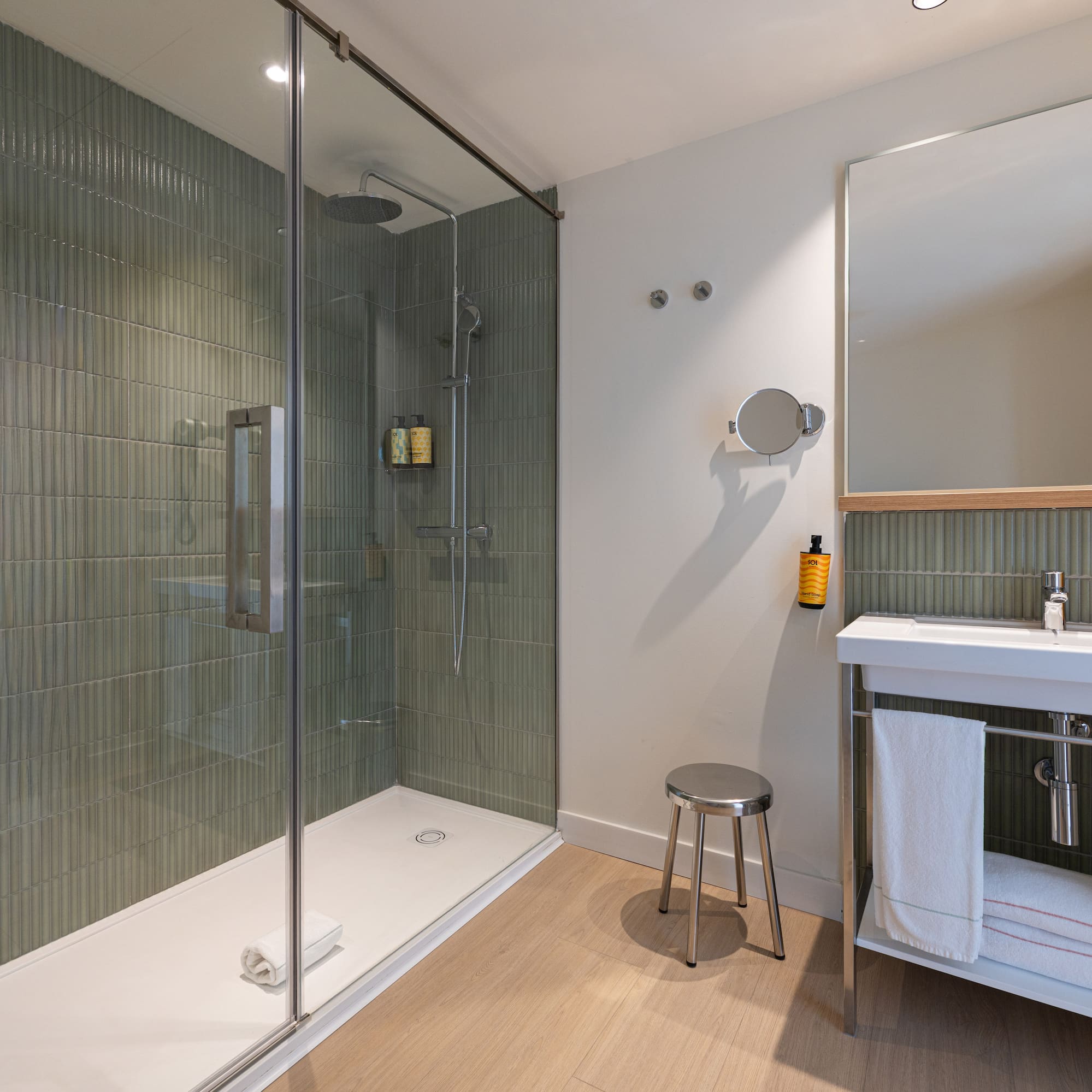 Modern bathroom with walk-in shower, green fluted tiles, white vanity sink, and mirror.