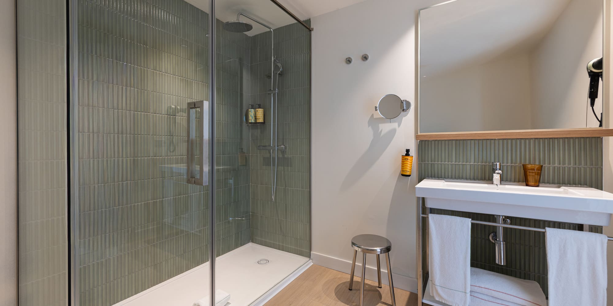 Modern bathroom with walk-in shower, green fluted tiles, white vanity sink, and mirror.