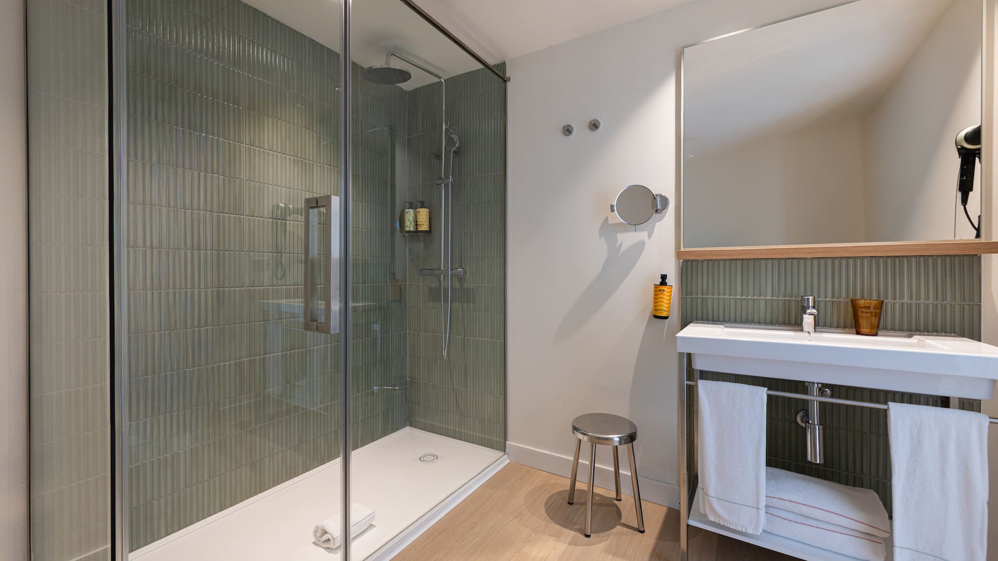 Modern bathroom with walk-in shower, green fluted tiles, white vanity sink, and mirror.