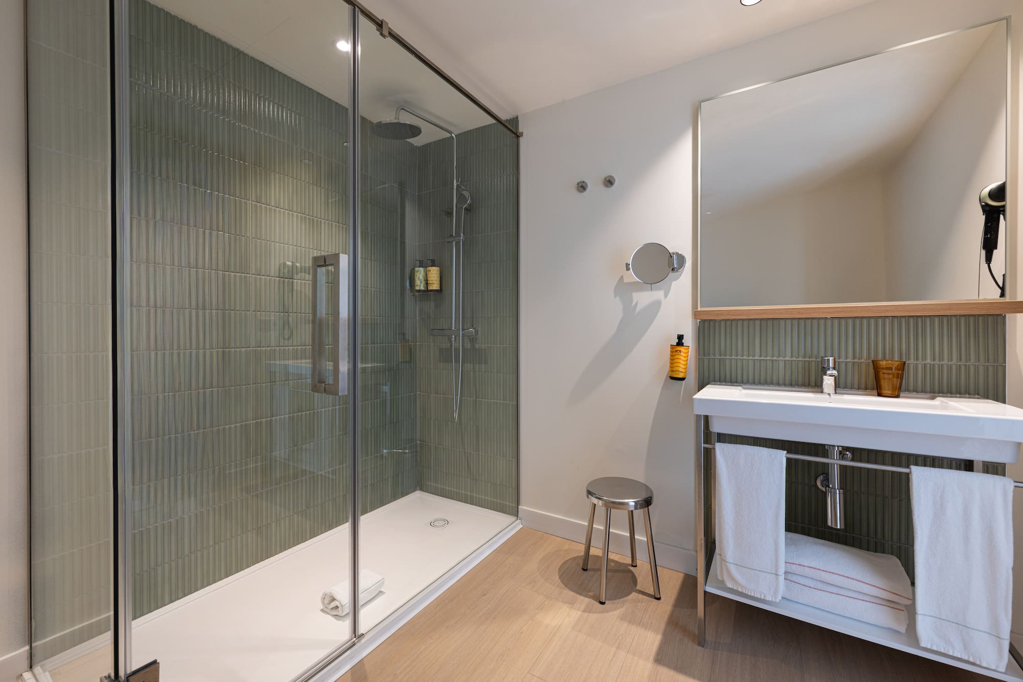 Modern bathroom featuring walk-in shower, green tile wall, white vanity, mirror.