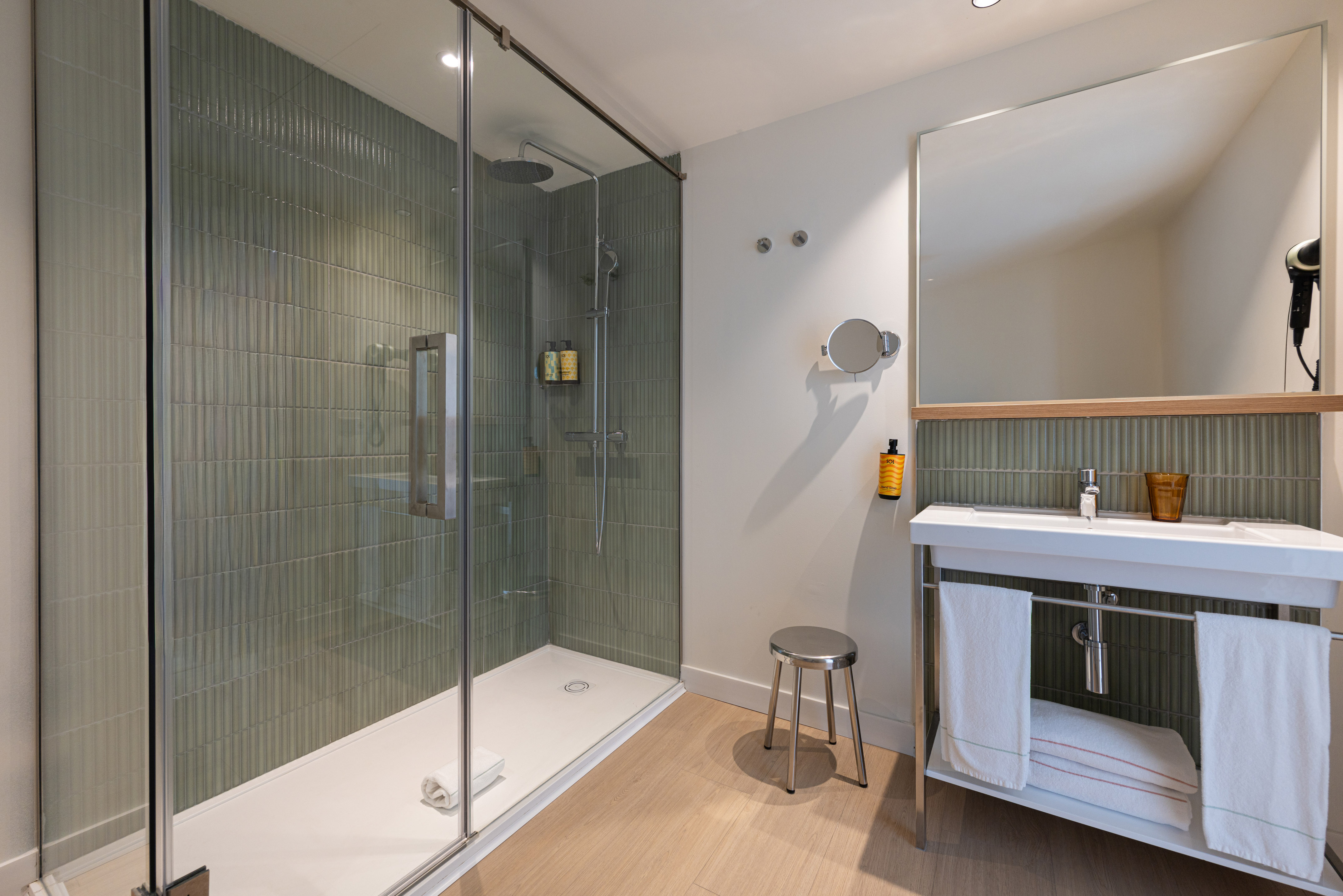 Modern bathroom featuring walk-in shower, green tile wall, white vanity, mirror.