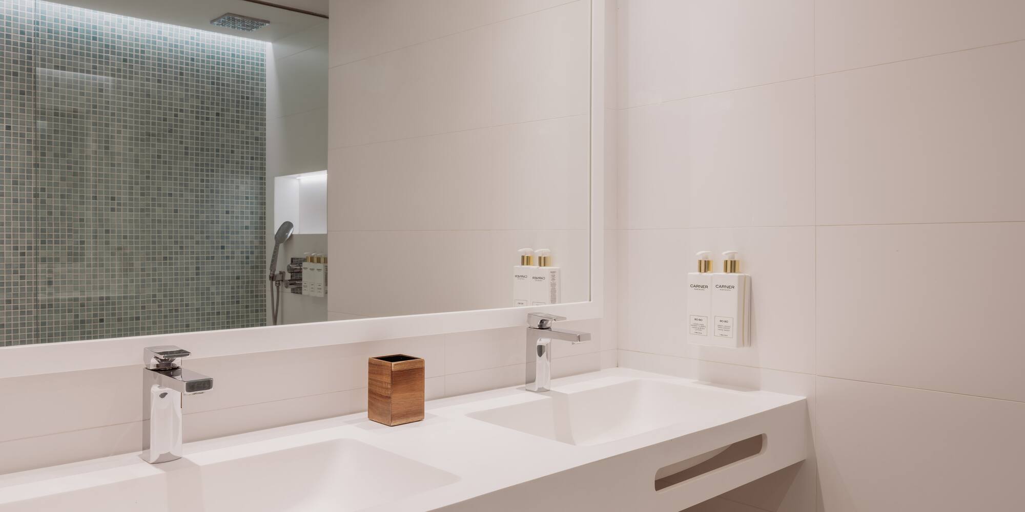 Baño moderno con lavabo doble blanco, grifos cromados y ducha de azulejos.