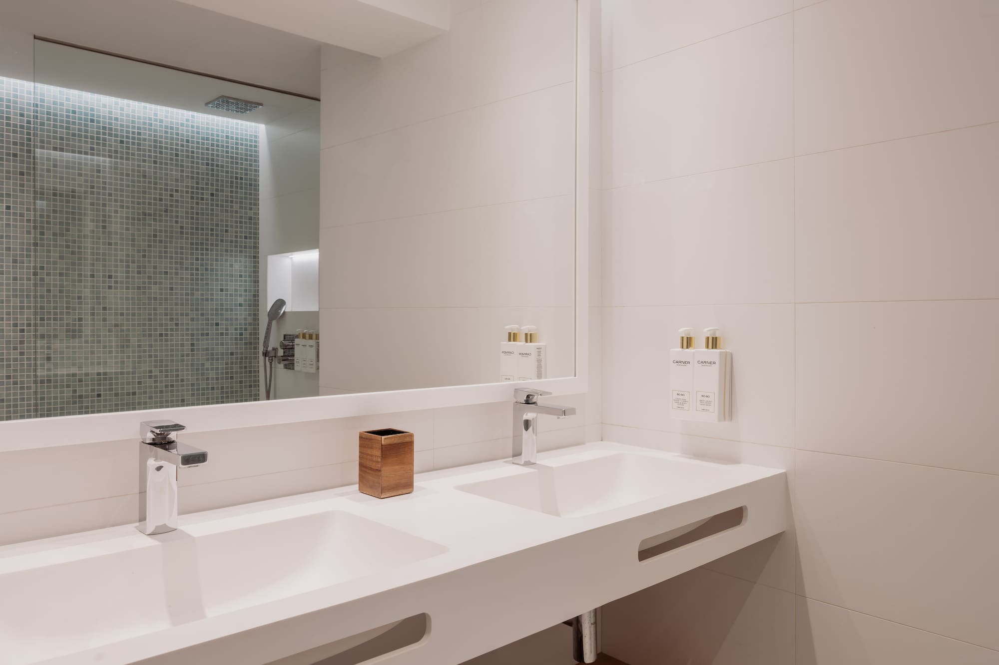Baño moderno con lavabo doble blanco, grifos cromados y ducha de azulejos.