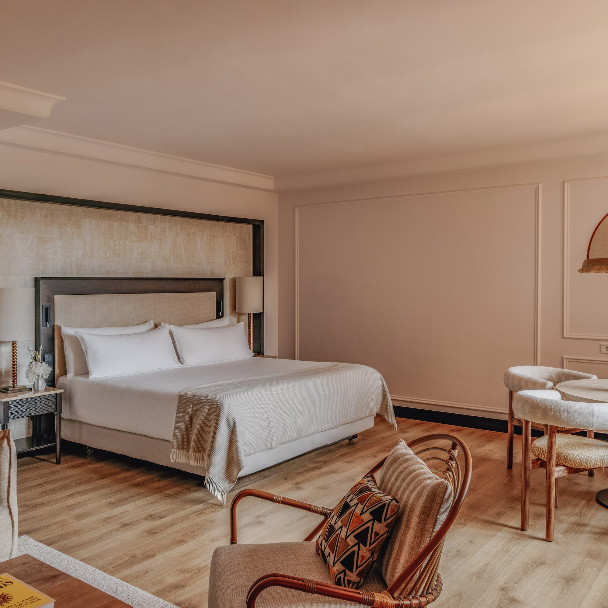 Luxury hotel suite with king bed, sofa lounge, and dining area, warm modern decor.