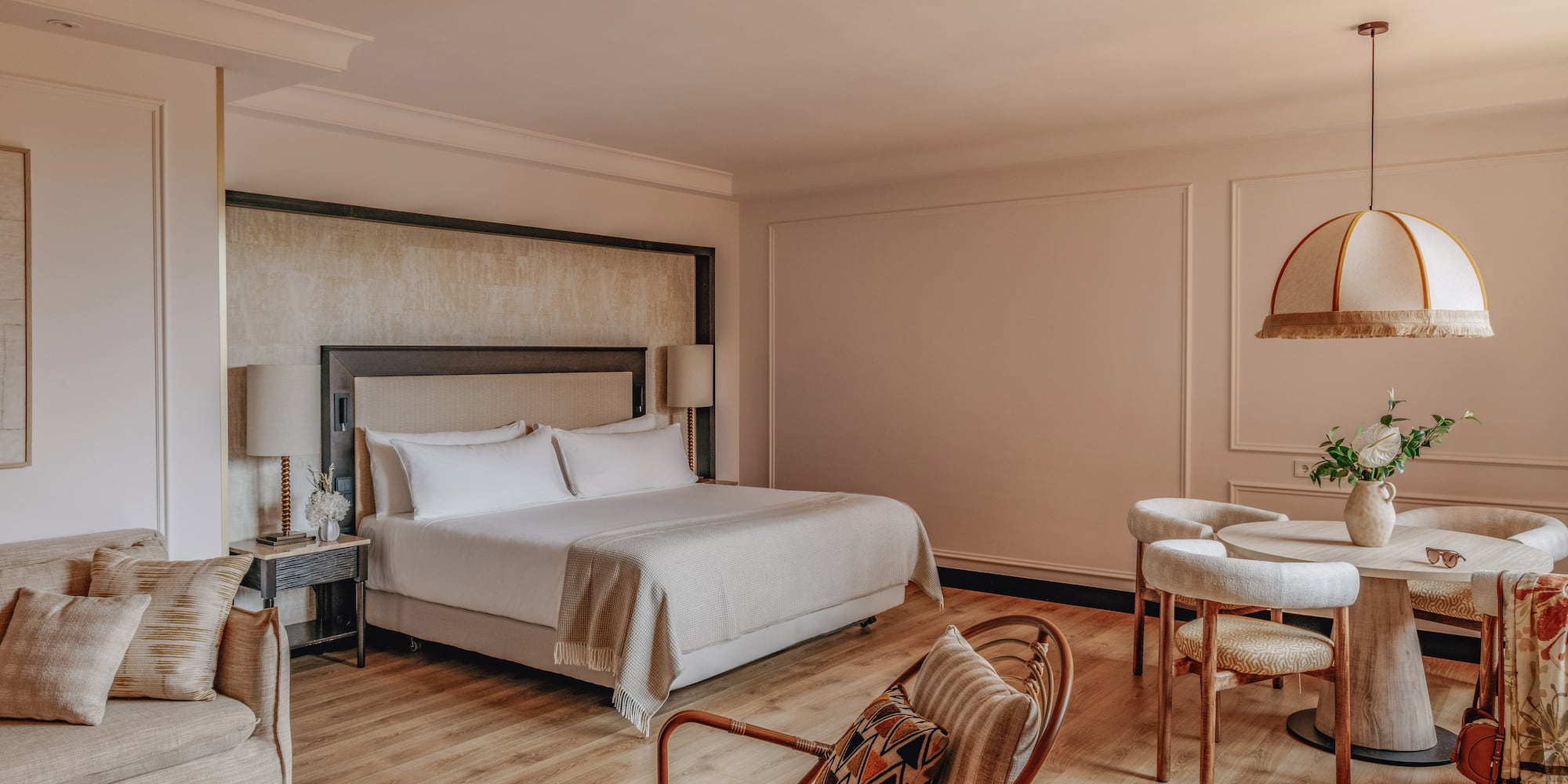 Luxury hotel suite with king bed, sofa lounge, and dining area, warm modern decor.