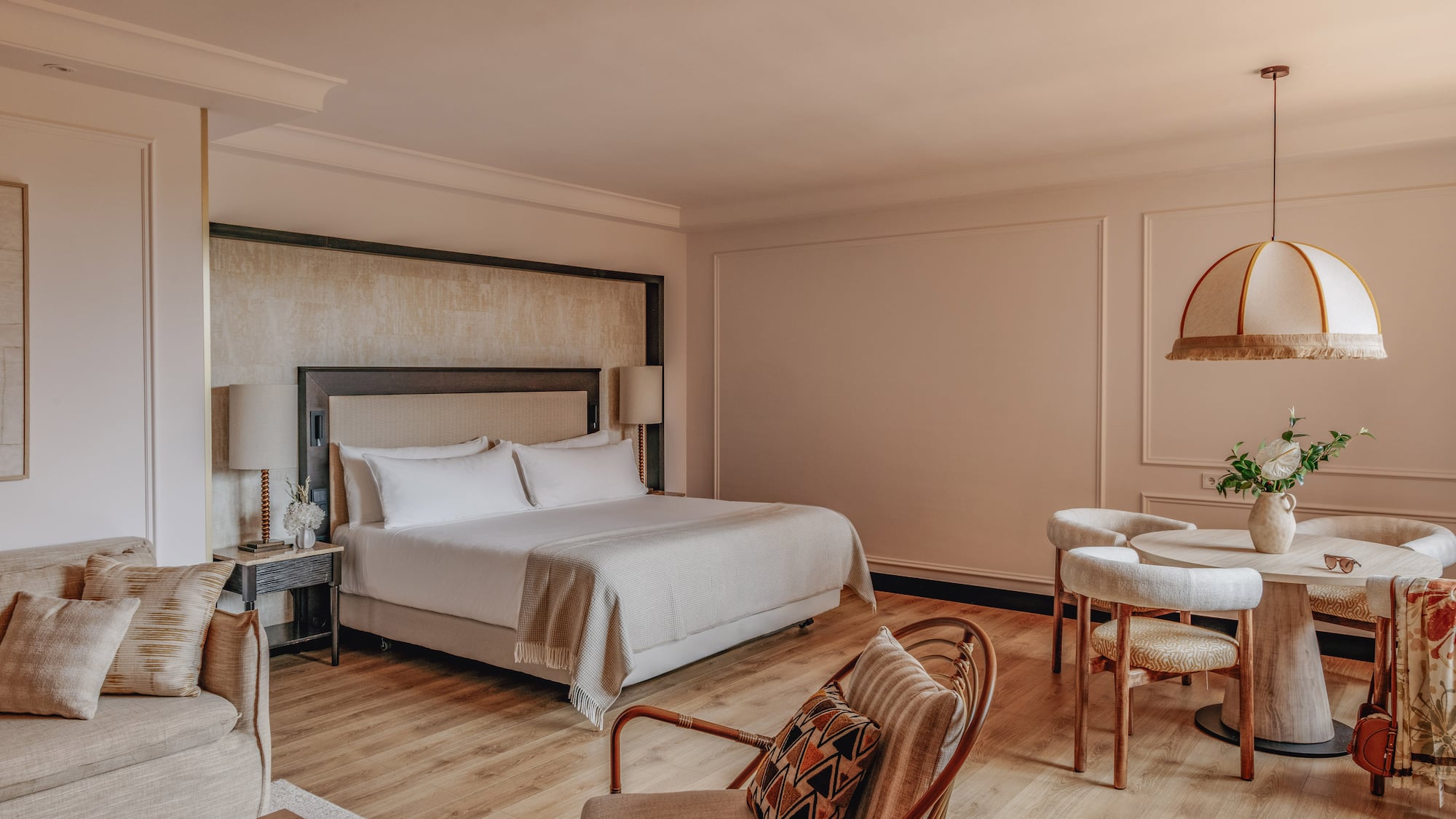 Luxury hotel suite with king bed, sofa lounge, and dining area, warm modern decor.