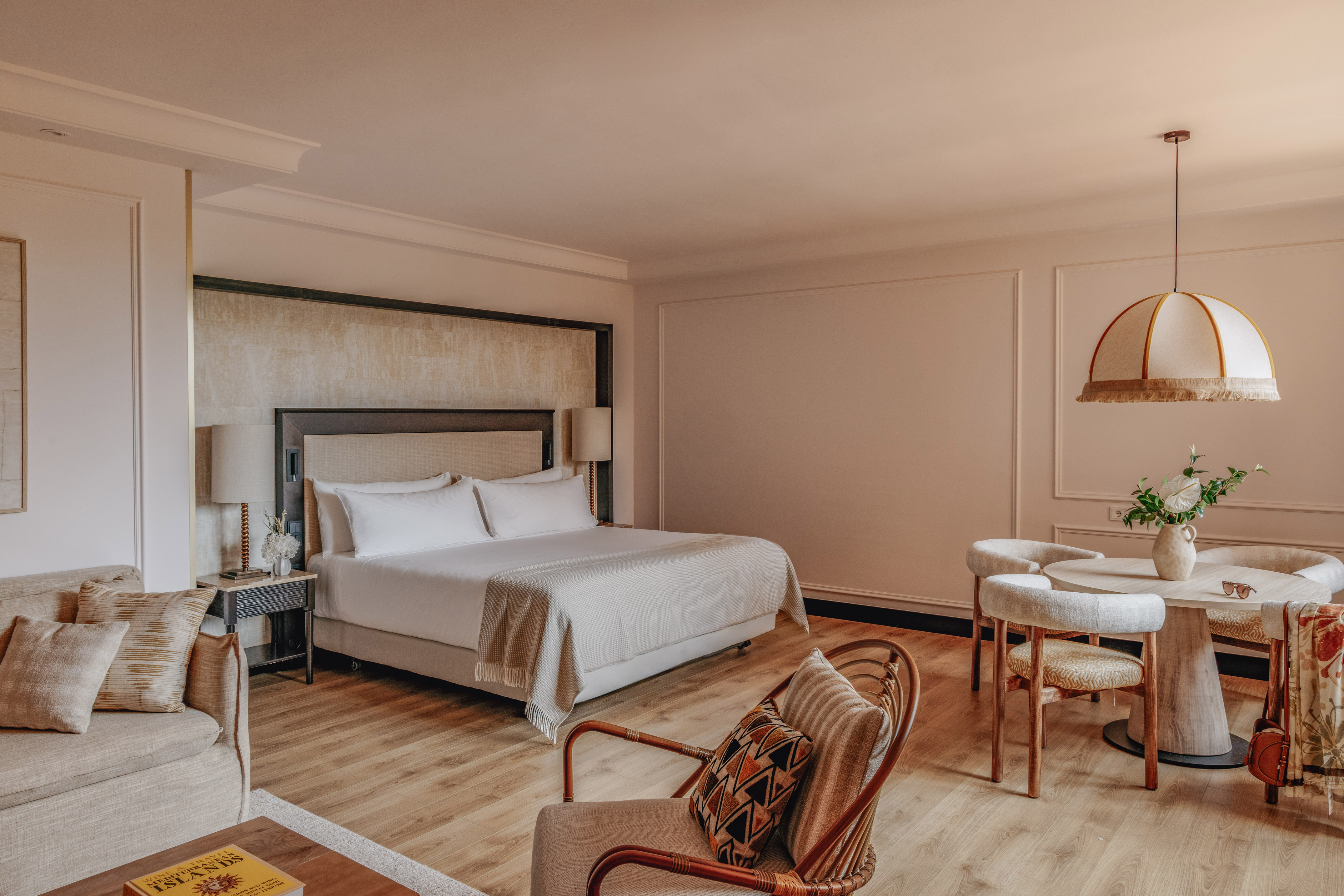 Luxury hotel suite with king bed, sofa lounge, and dining area, warm modern decor.
