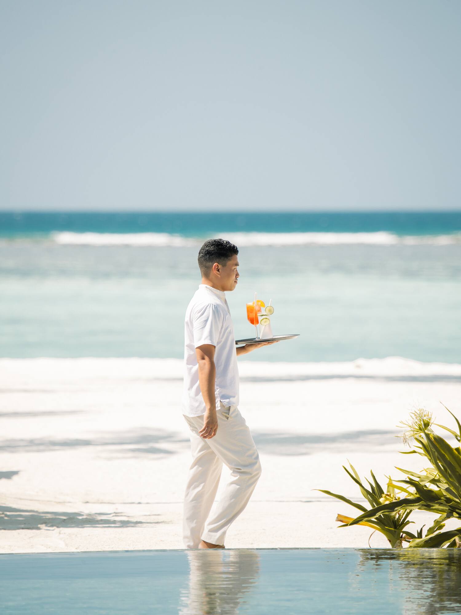 a man carrying a tray with a drink on a beach
