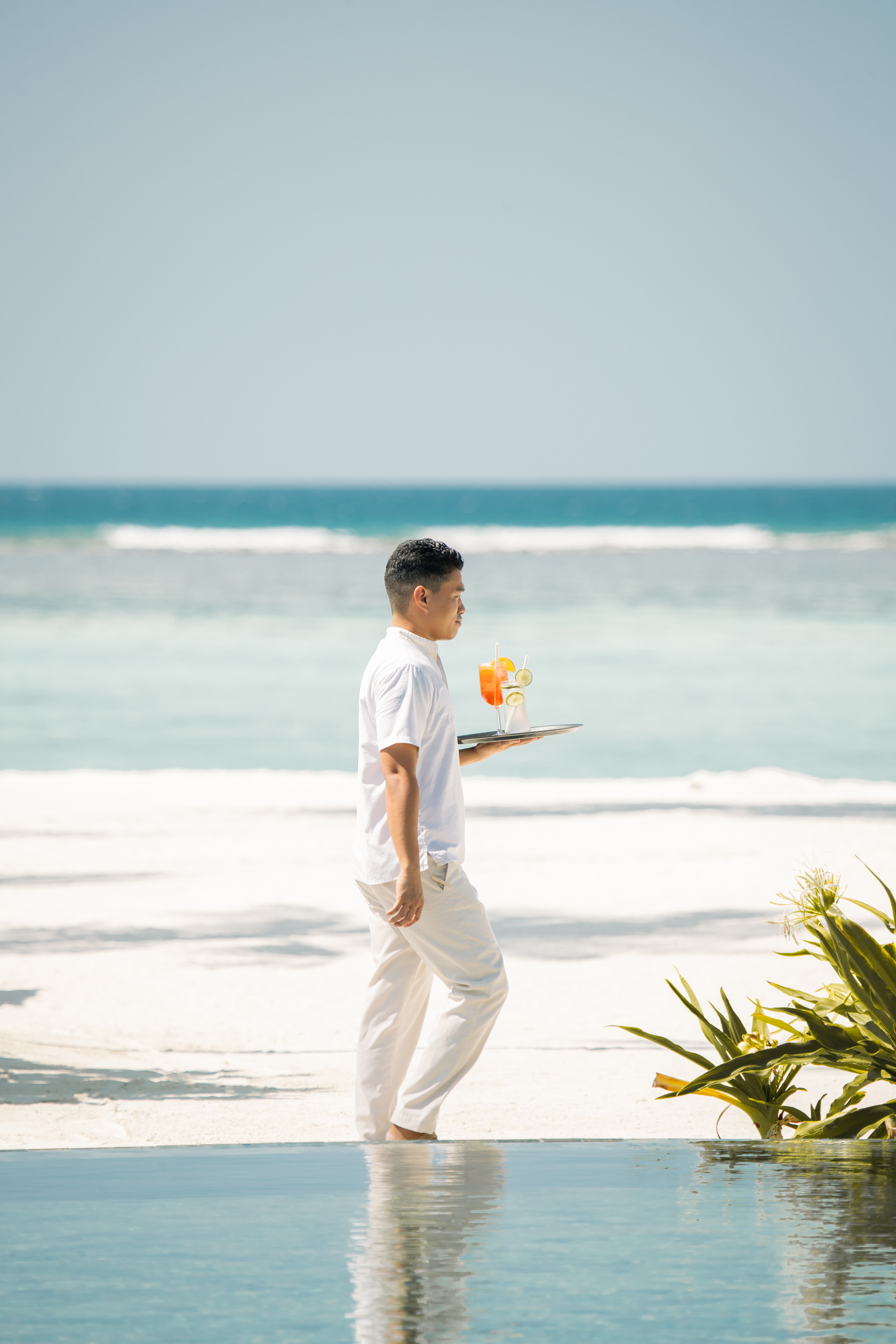 a man carrying a tray with a drink on a beach
