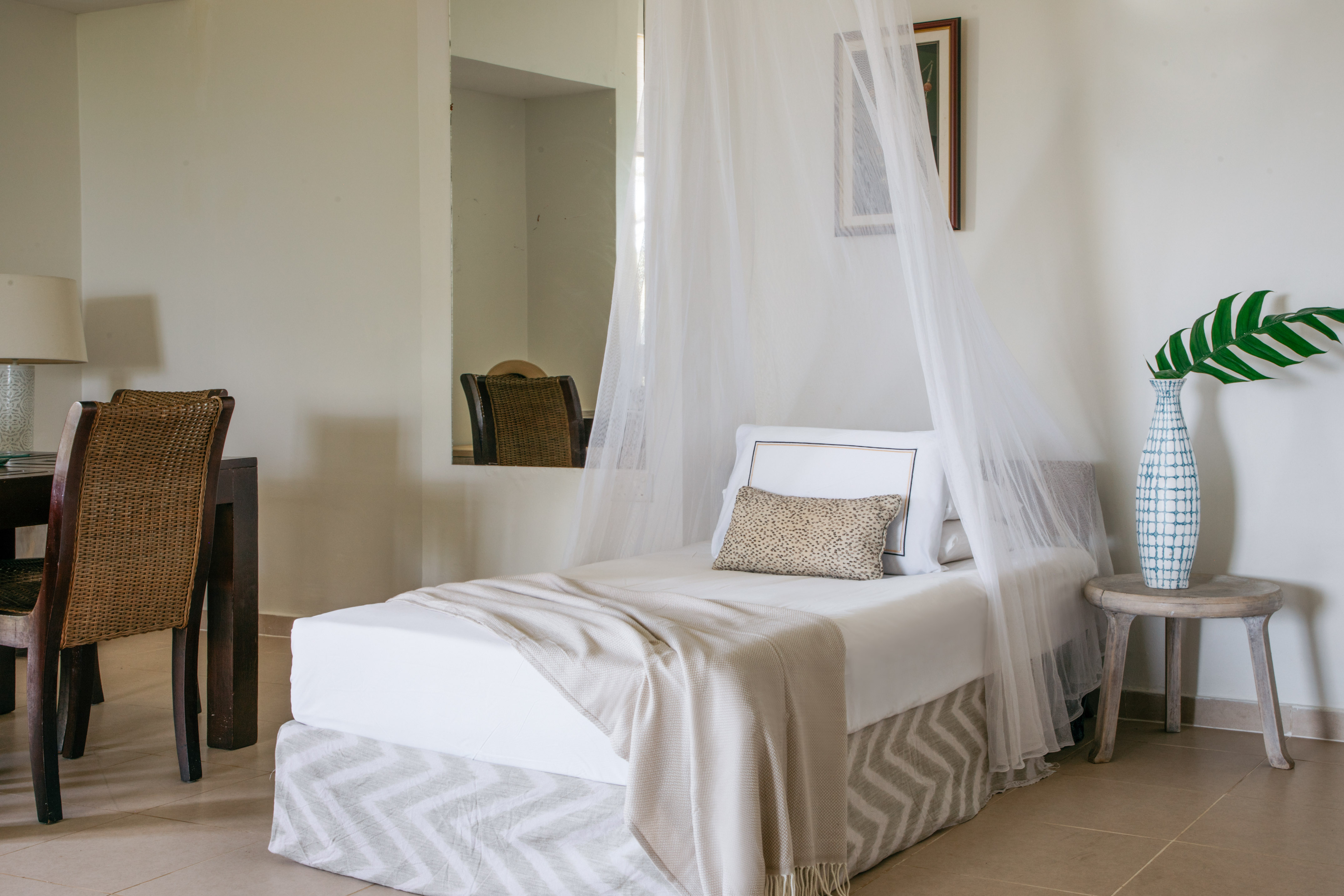 White single canopy bed with chevron skirt and tropical plant decor.
