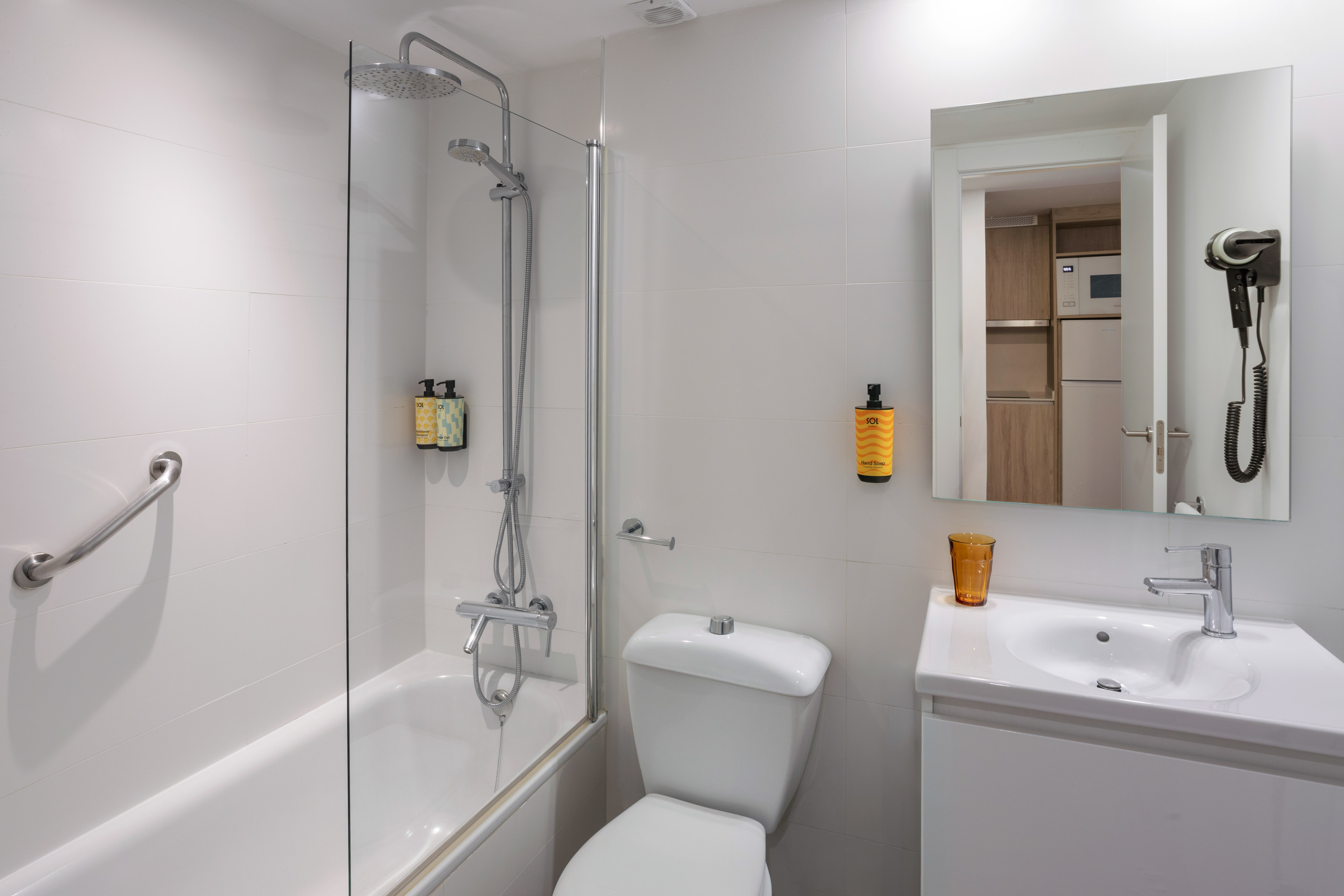 White modern bathroom with shower-bathtub, toilet, sink, mirror, and hairdryer.