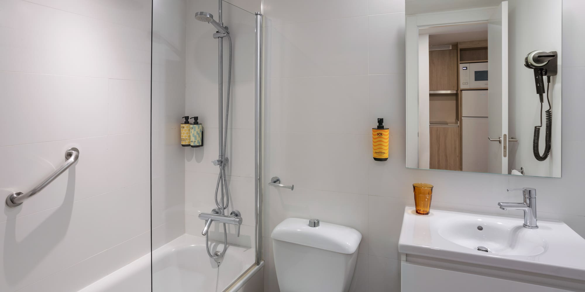 Hotel bathroom: white tiles, shower-bathtub, toilet, sink, mirror, hairdryer.