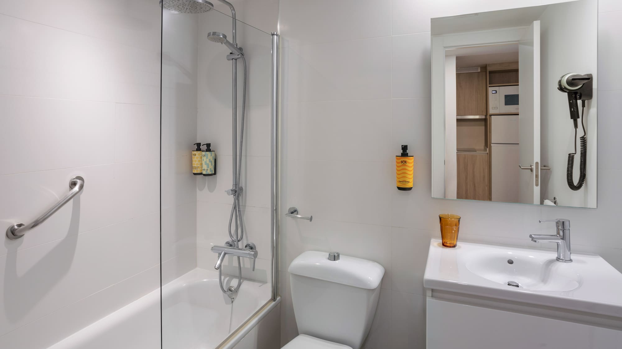 Hotel bathroom: white tiles, shower-bathtub, toilet, sink, mirror, hairdryer.