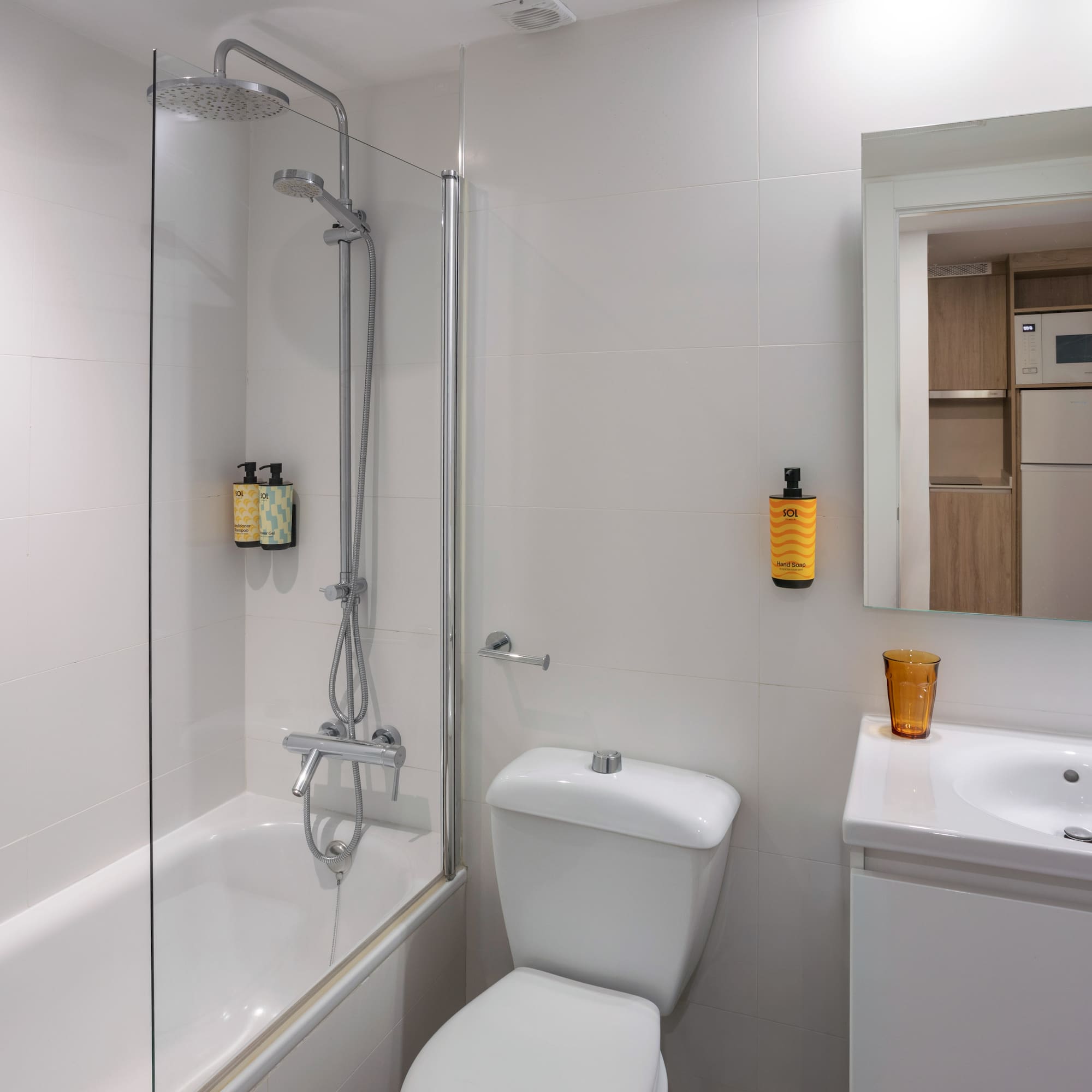 Hotel bathroom: white tiles, shower-bathtub, toilet, sink, mirror, hairdryer.