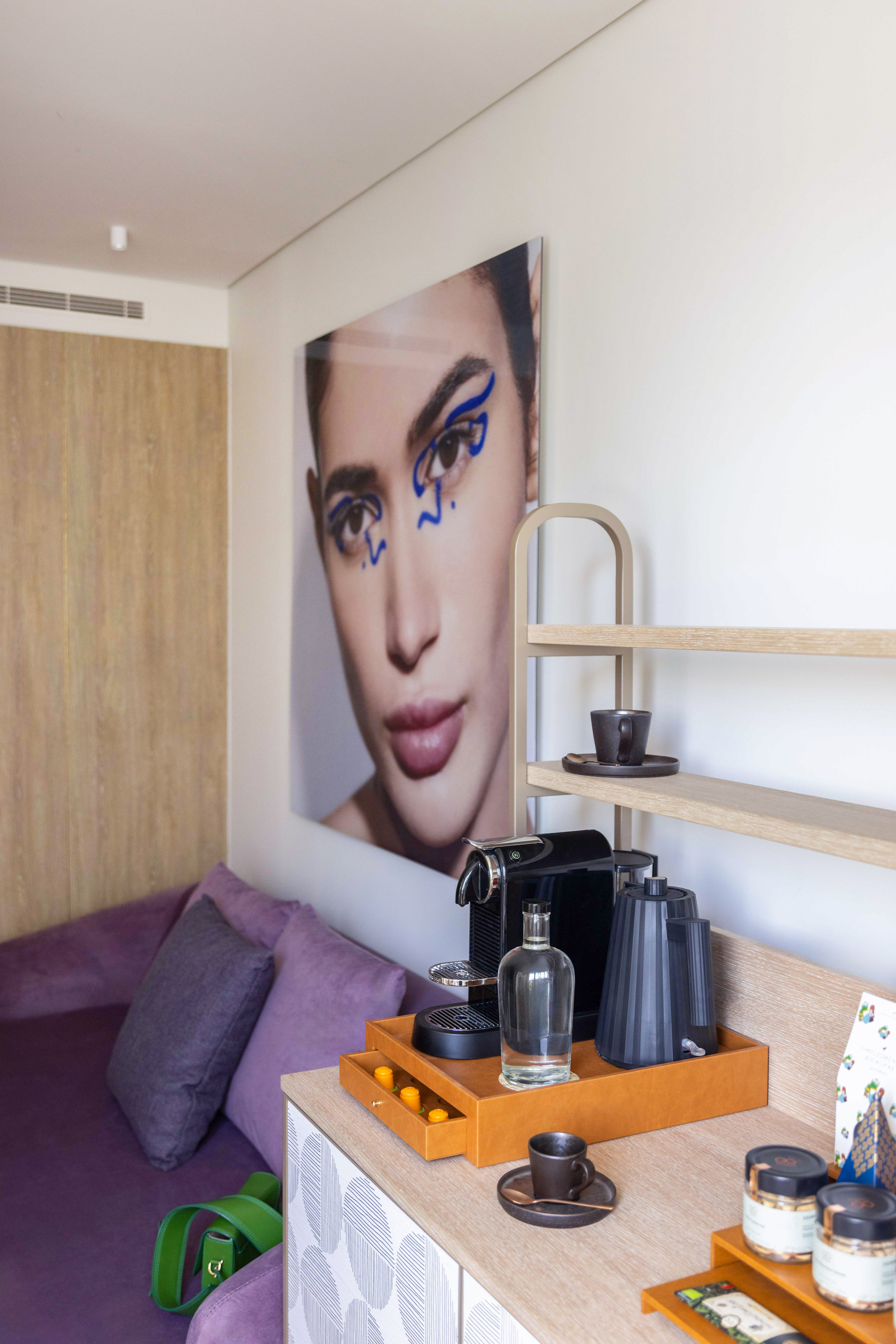 Modern hotel room with Nespresso coffee station, purple sofa, and abstract art print.