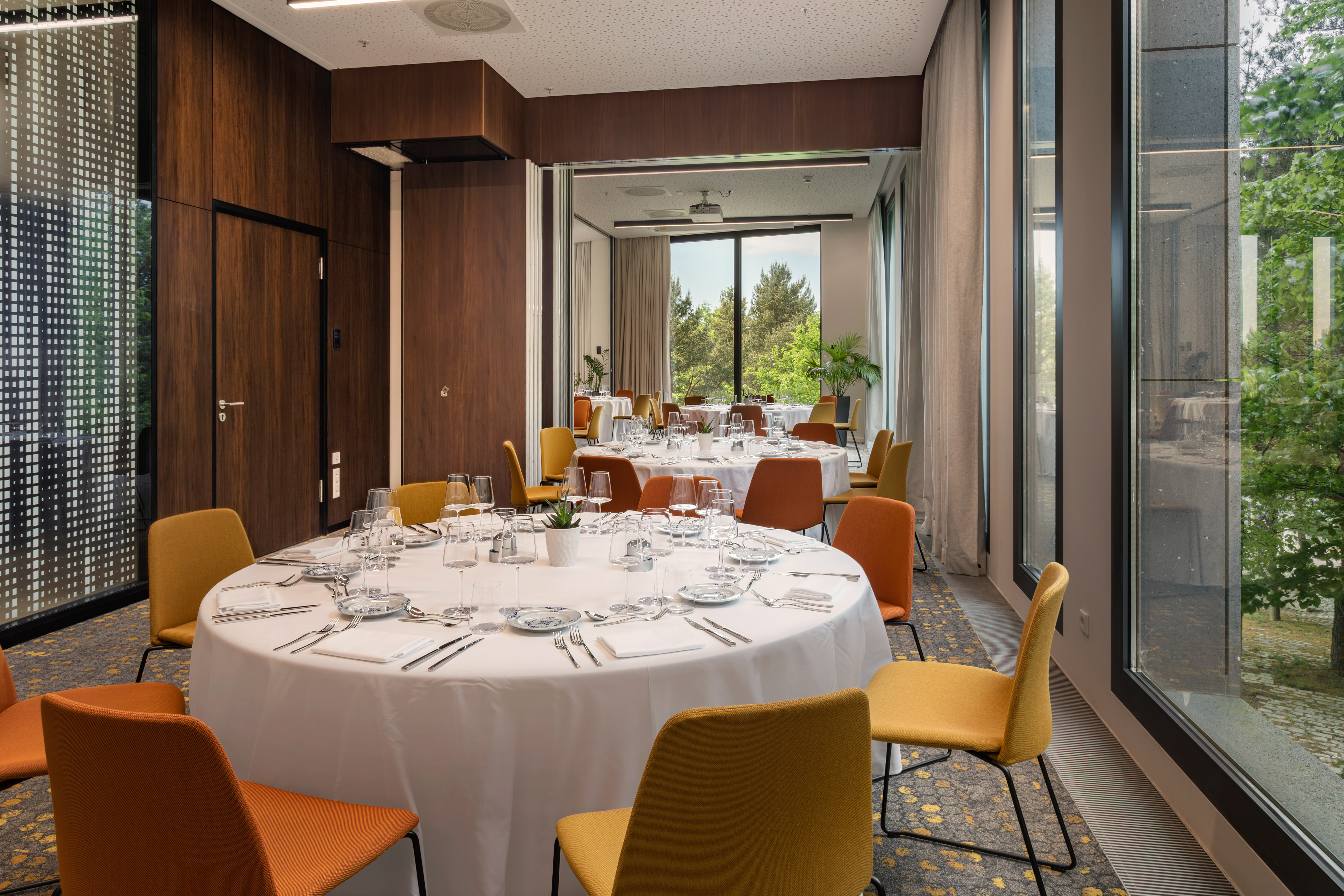 Modern conference room with round tables, colorful chairs, and forest view.