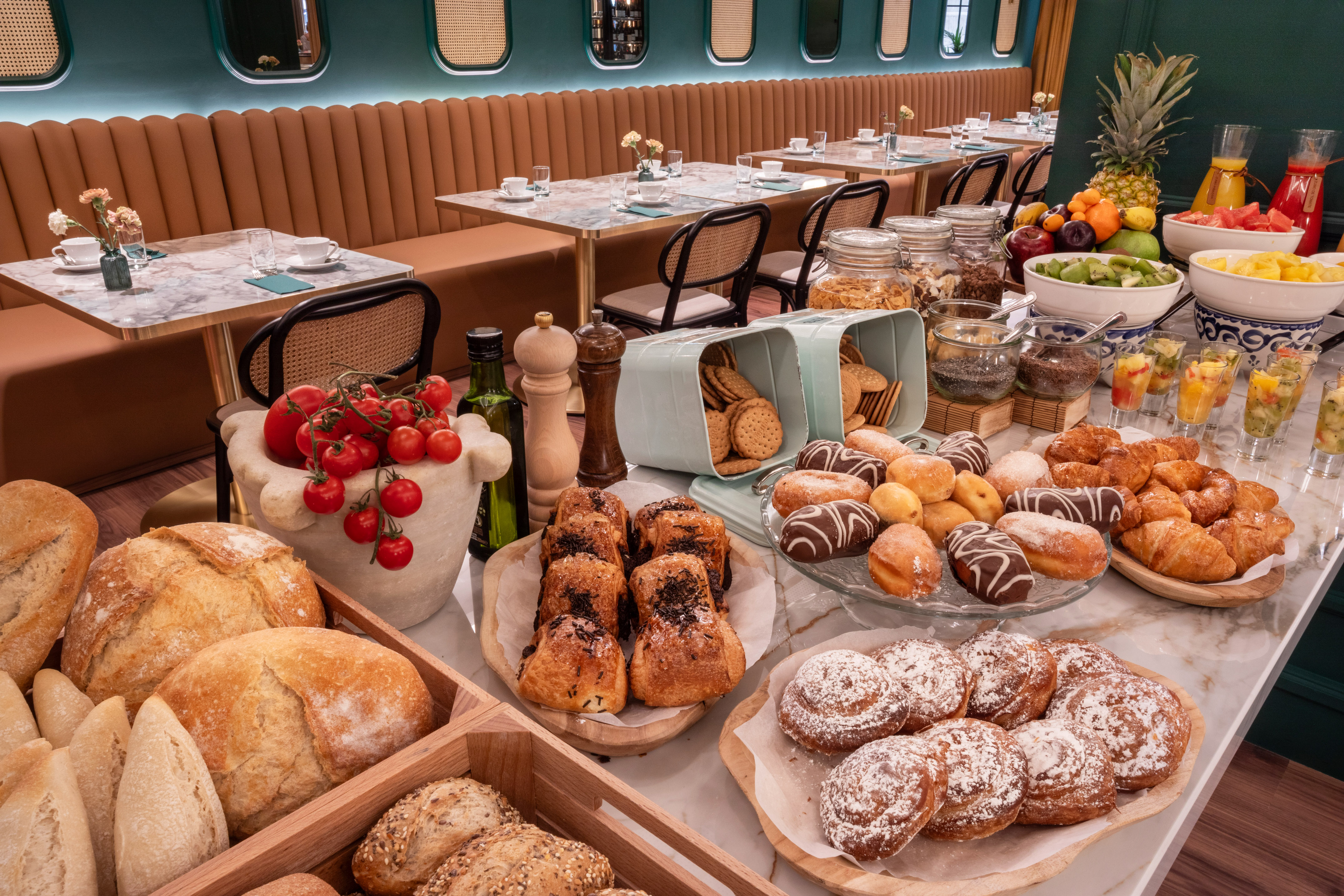 Hotel breakfast buffet with fresh fruit, pastries, bread, and juices on a marble counter.