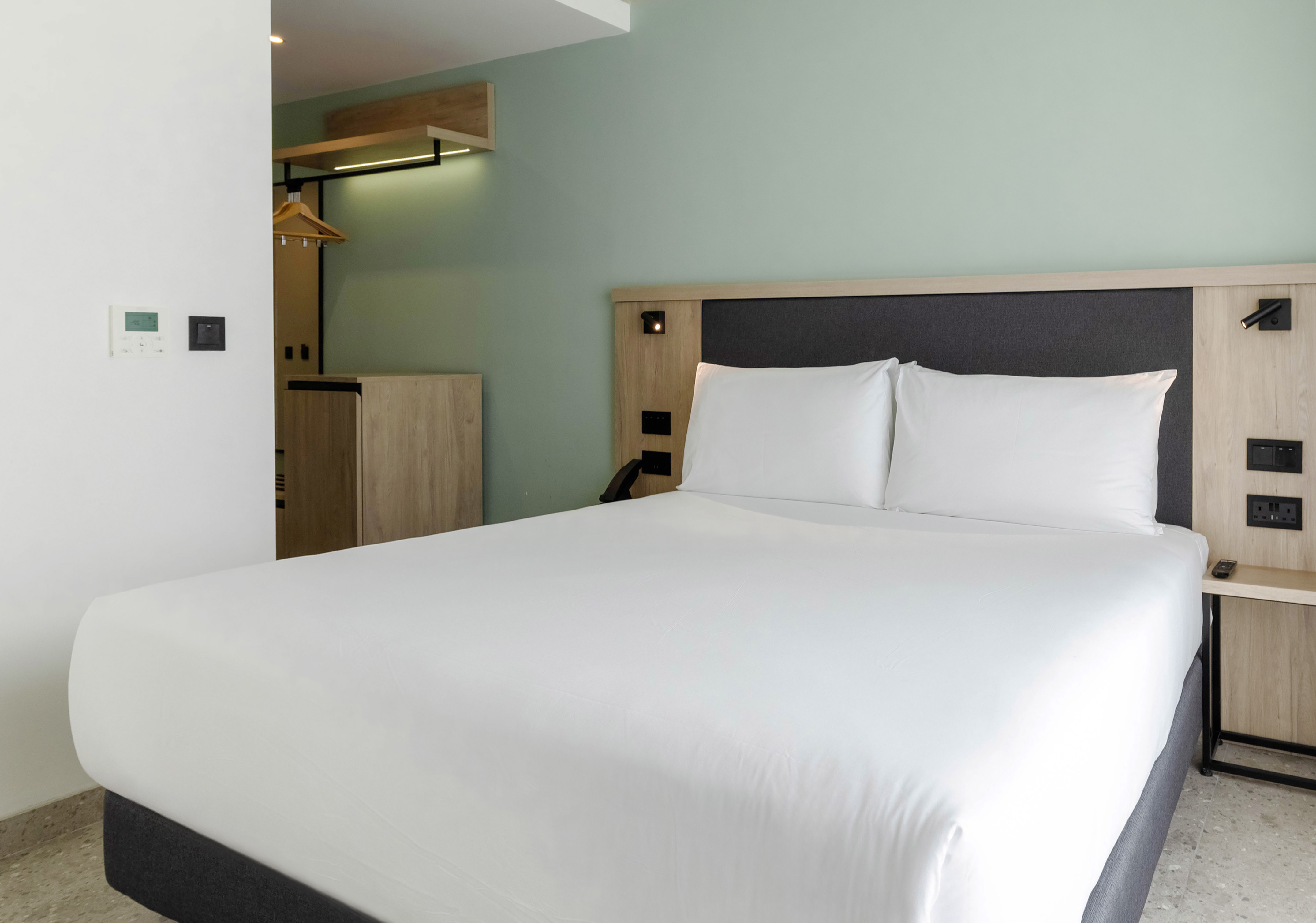 Clean hotel room interior with queen bed, white sheets, wood trim, and green wall.