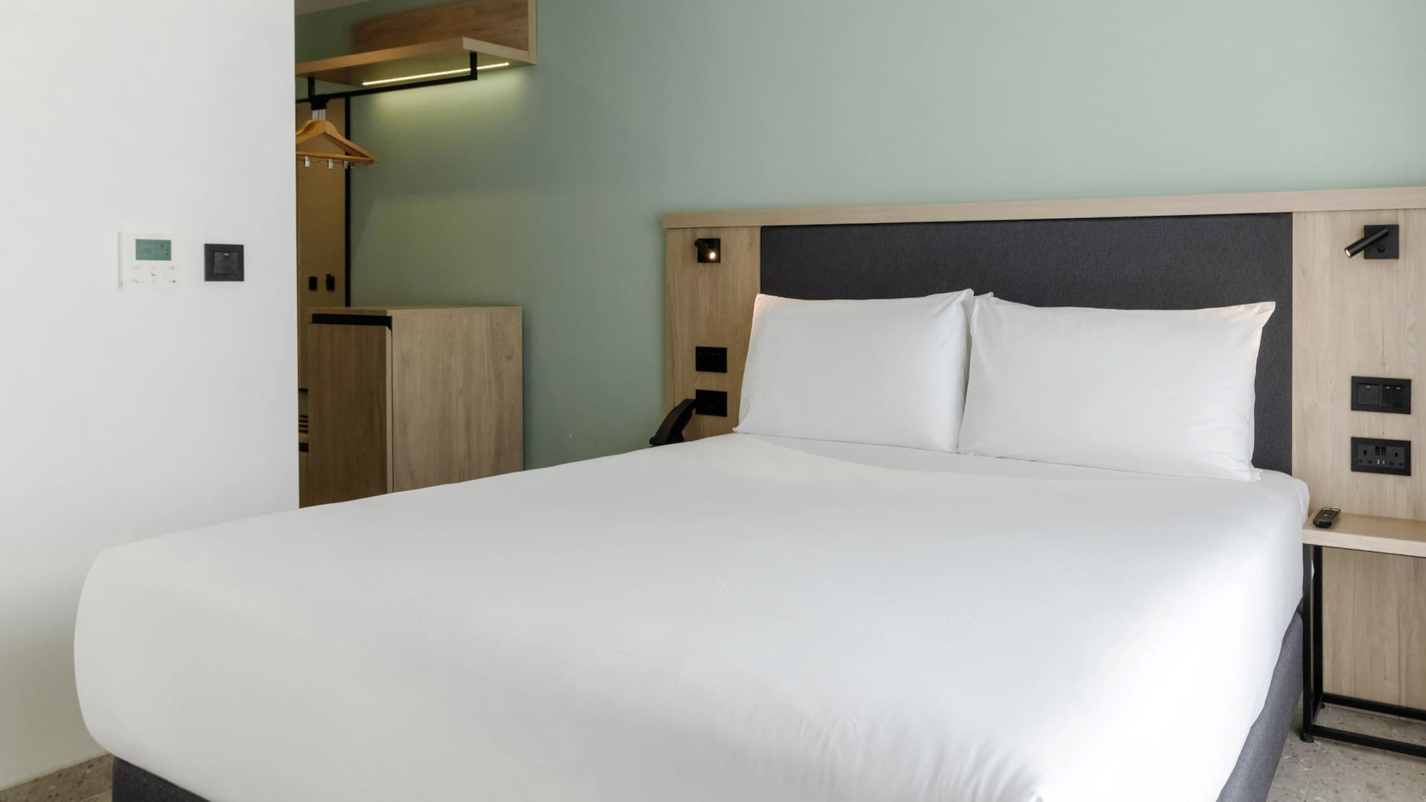 Clean hotel room interior with queen bed, white sheets, wood trim, and green wall.