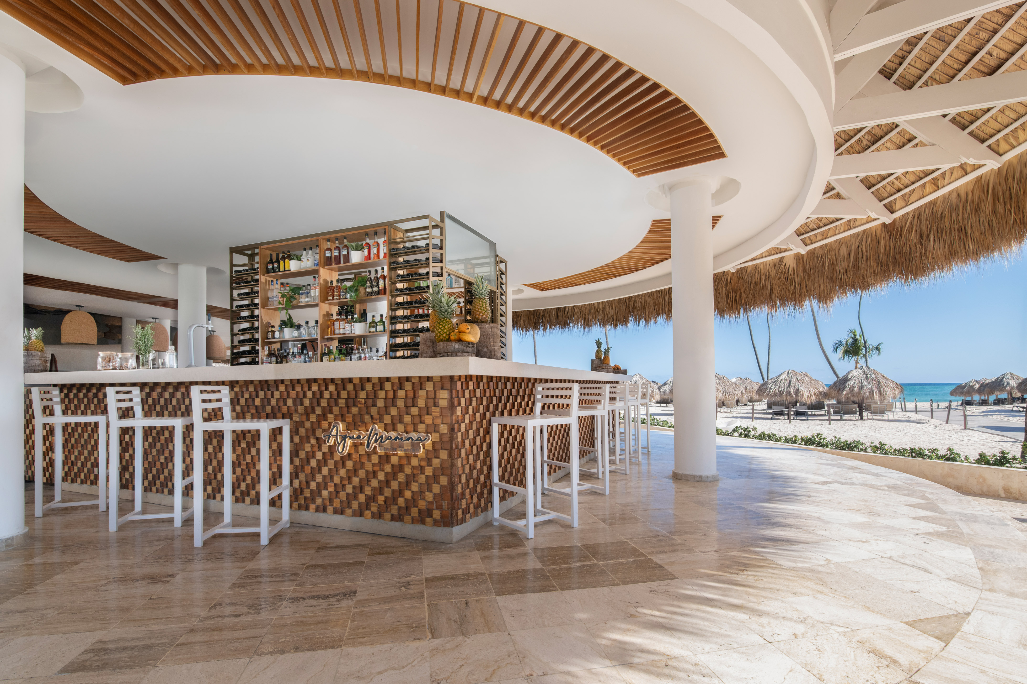 Agua Marina beach bar with white stools, wooden counter, and clear ocean view.
