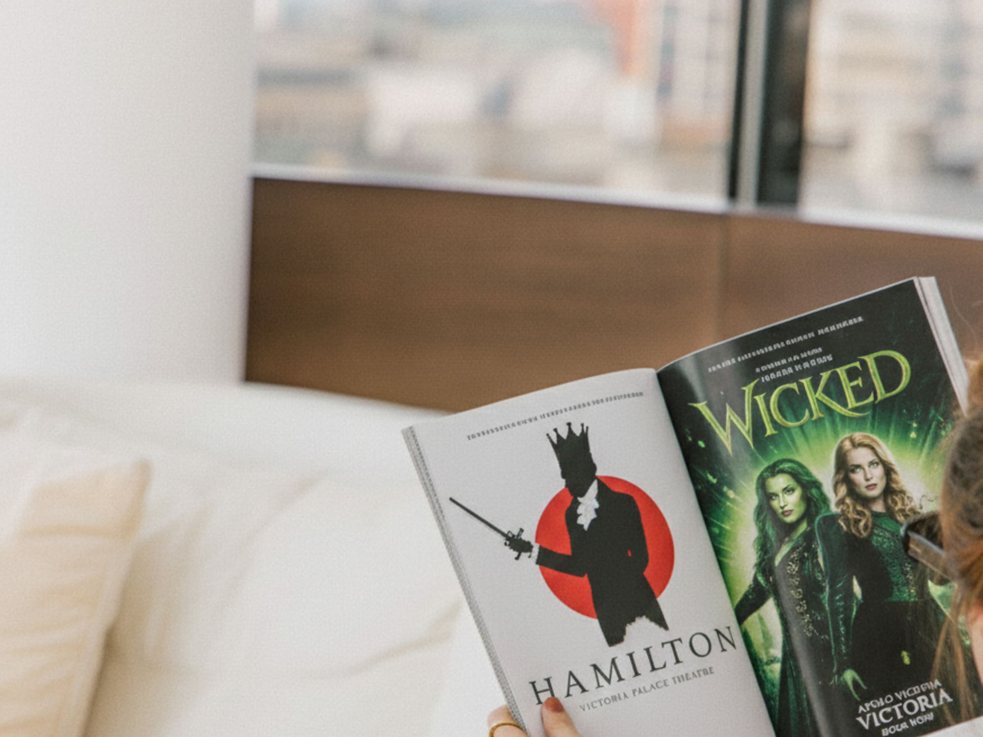 Person reading a magazine featuring Hamilton and Wicked musicals.