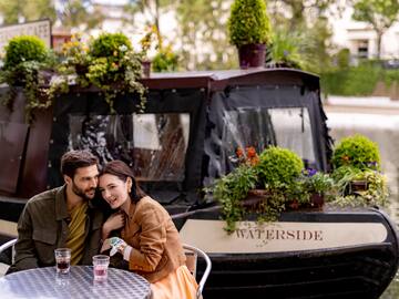 a man and woman sitting at a table with plants on the side of them