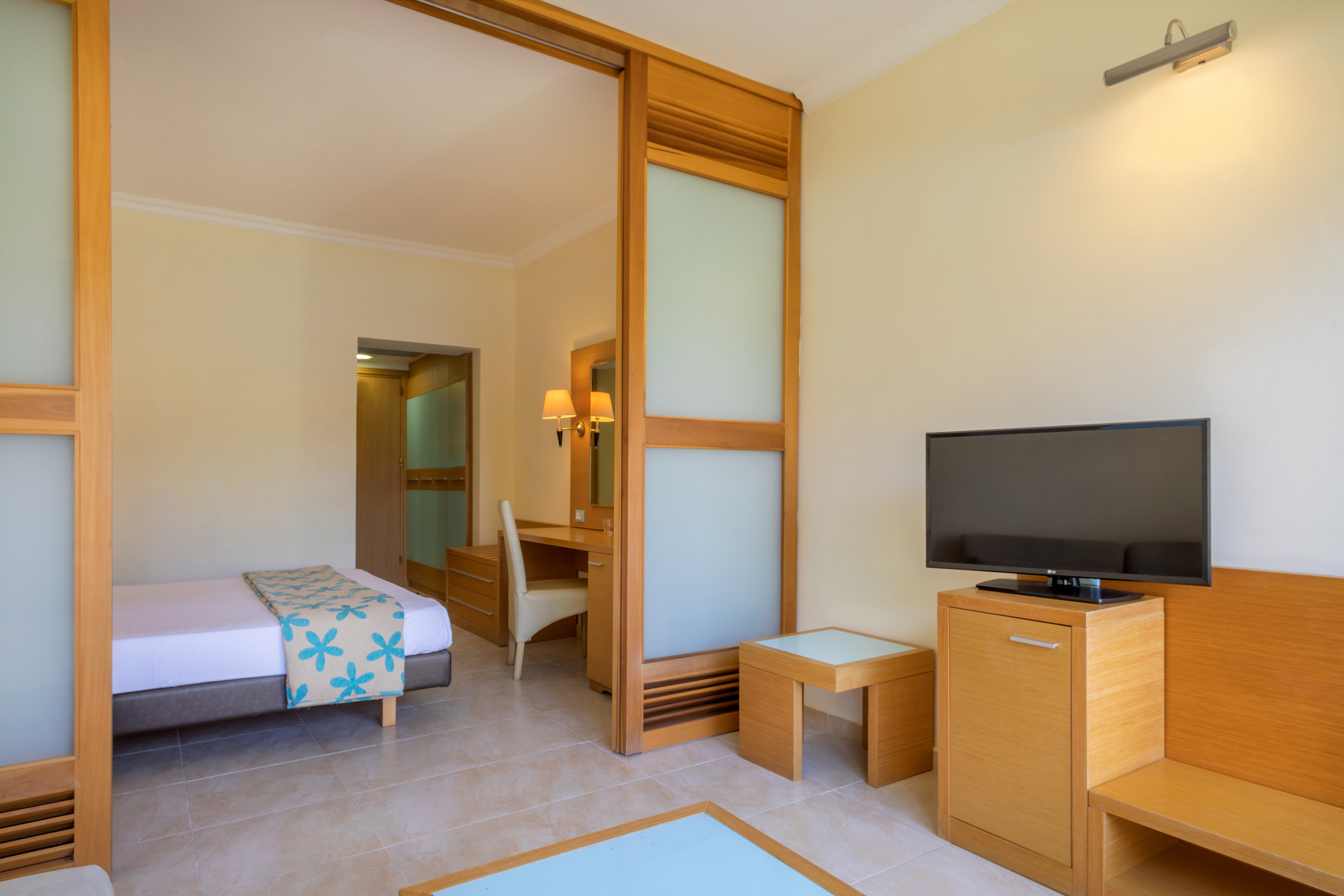 Modern hotel room with single bed, desk, flat-screen TV, and wooden room divider.