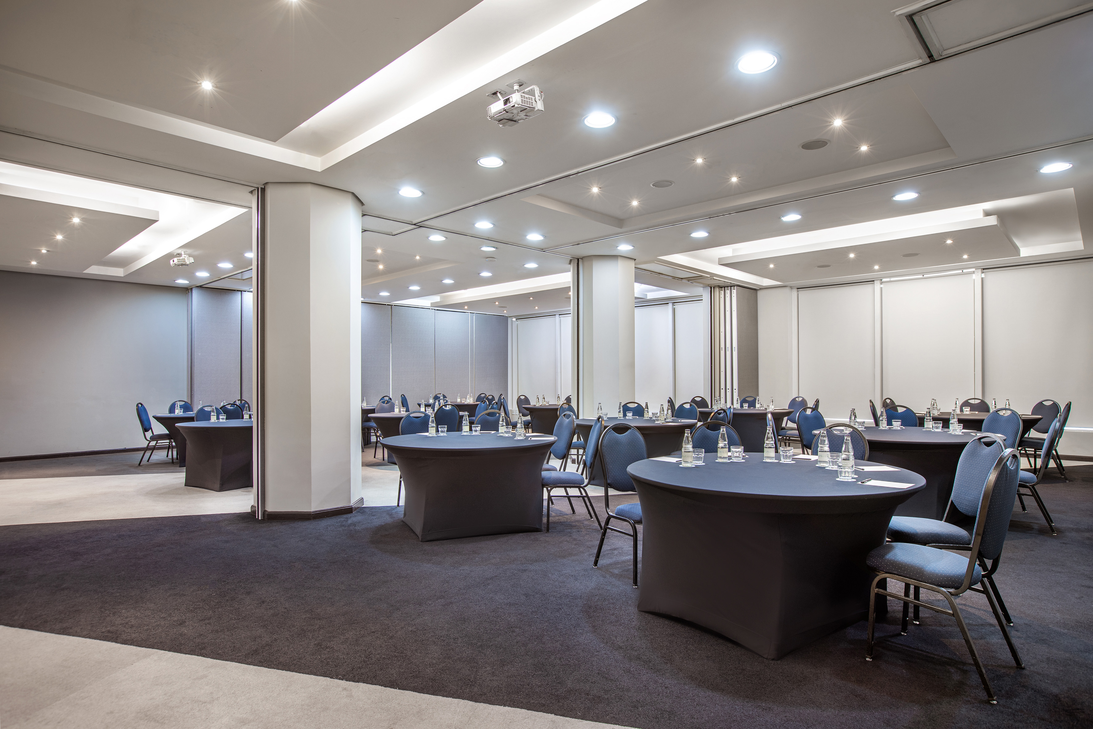 Modern conference room with round tables, blue chairs, and ceiling projector.