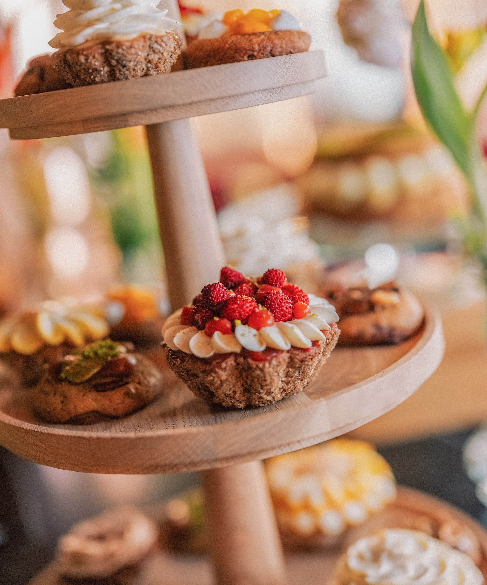 Wooden tiered stand with assorted mini tarts, wild strawberry tart in focus.