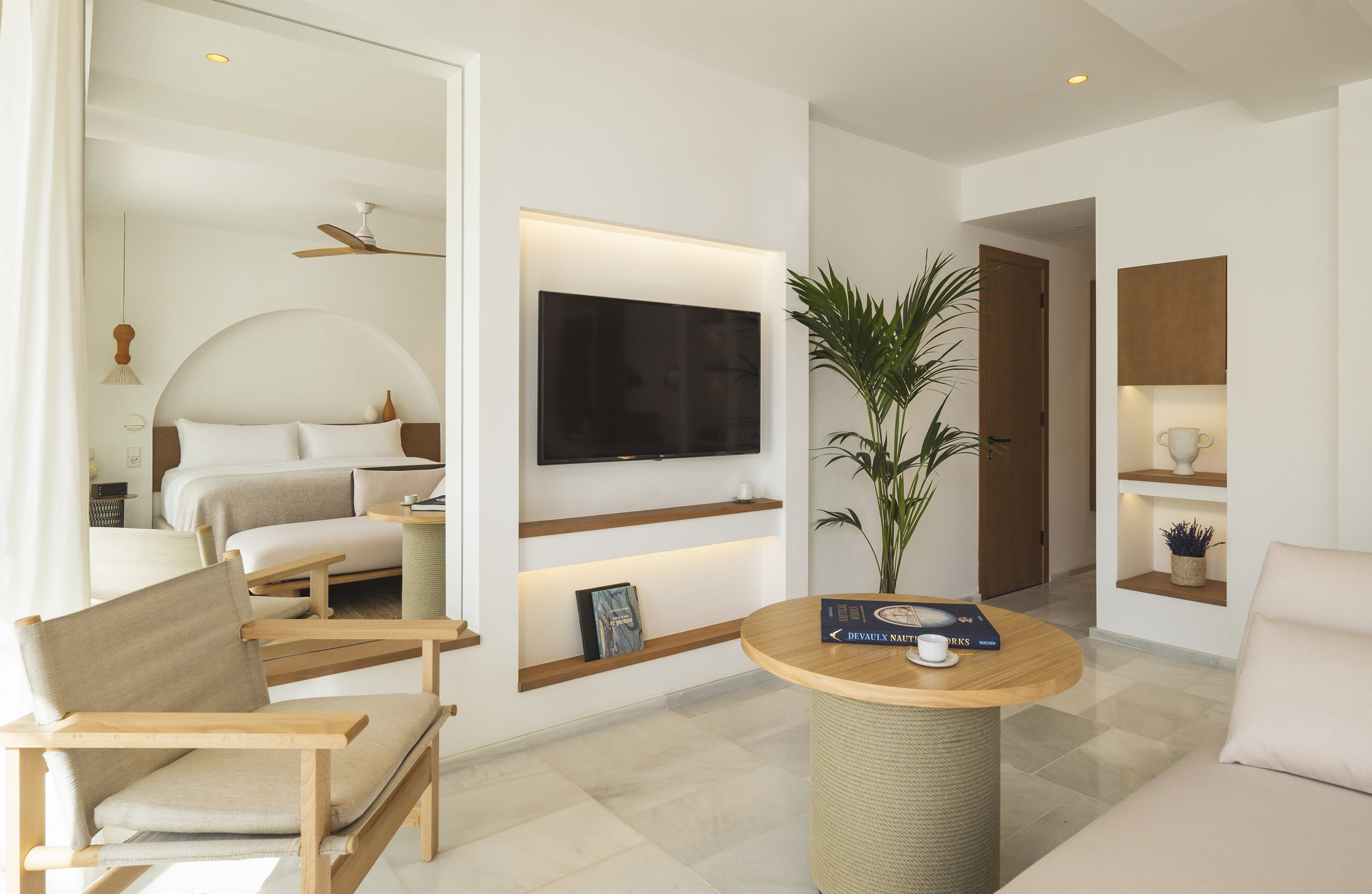 Modern hotel suite living room and bedroom with light, minimalist decor.