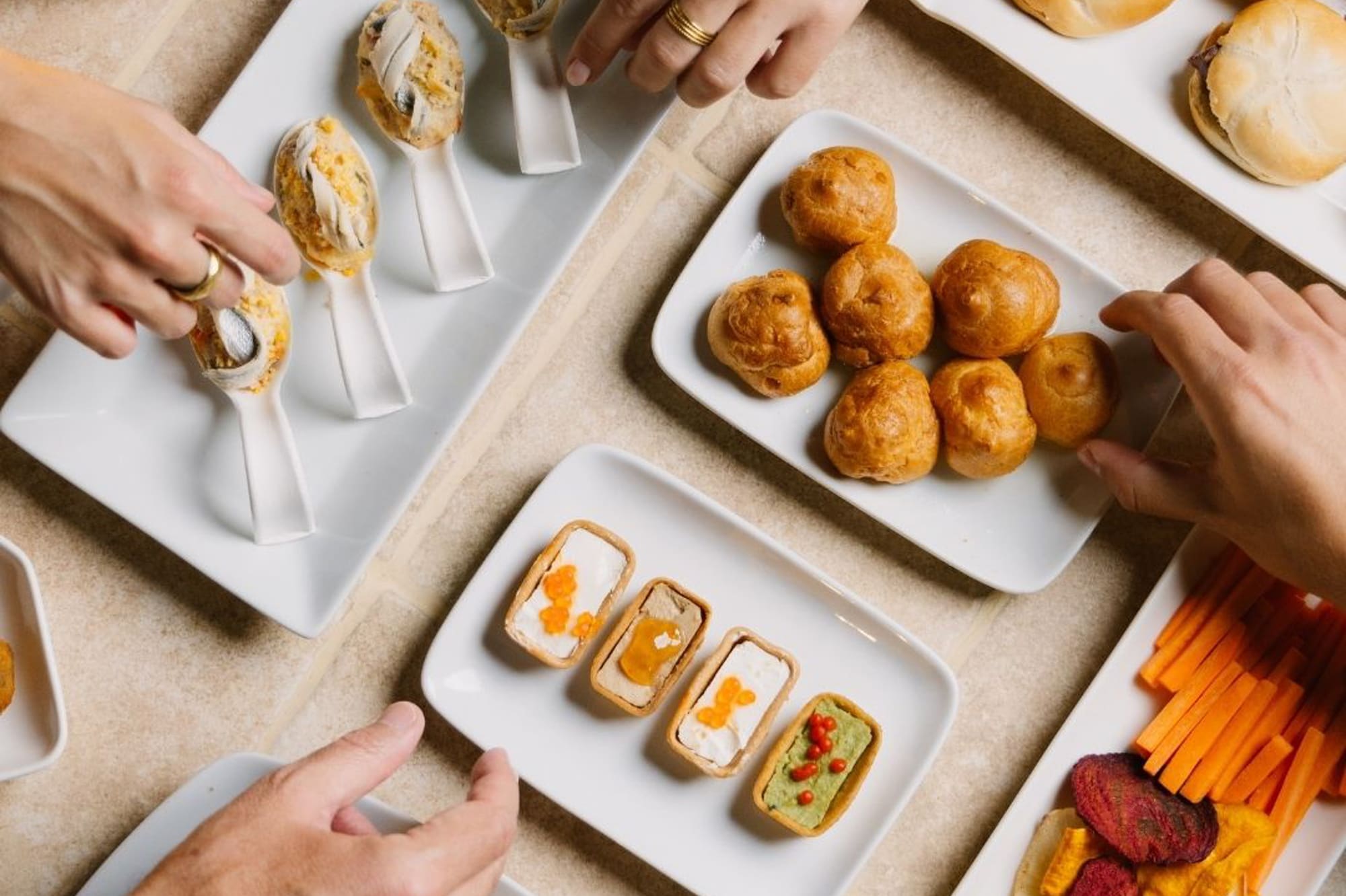 Hands reaching for elegant canapés, mini sandwiches, and gourmet appetizers.