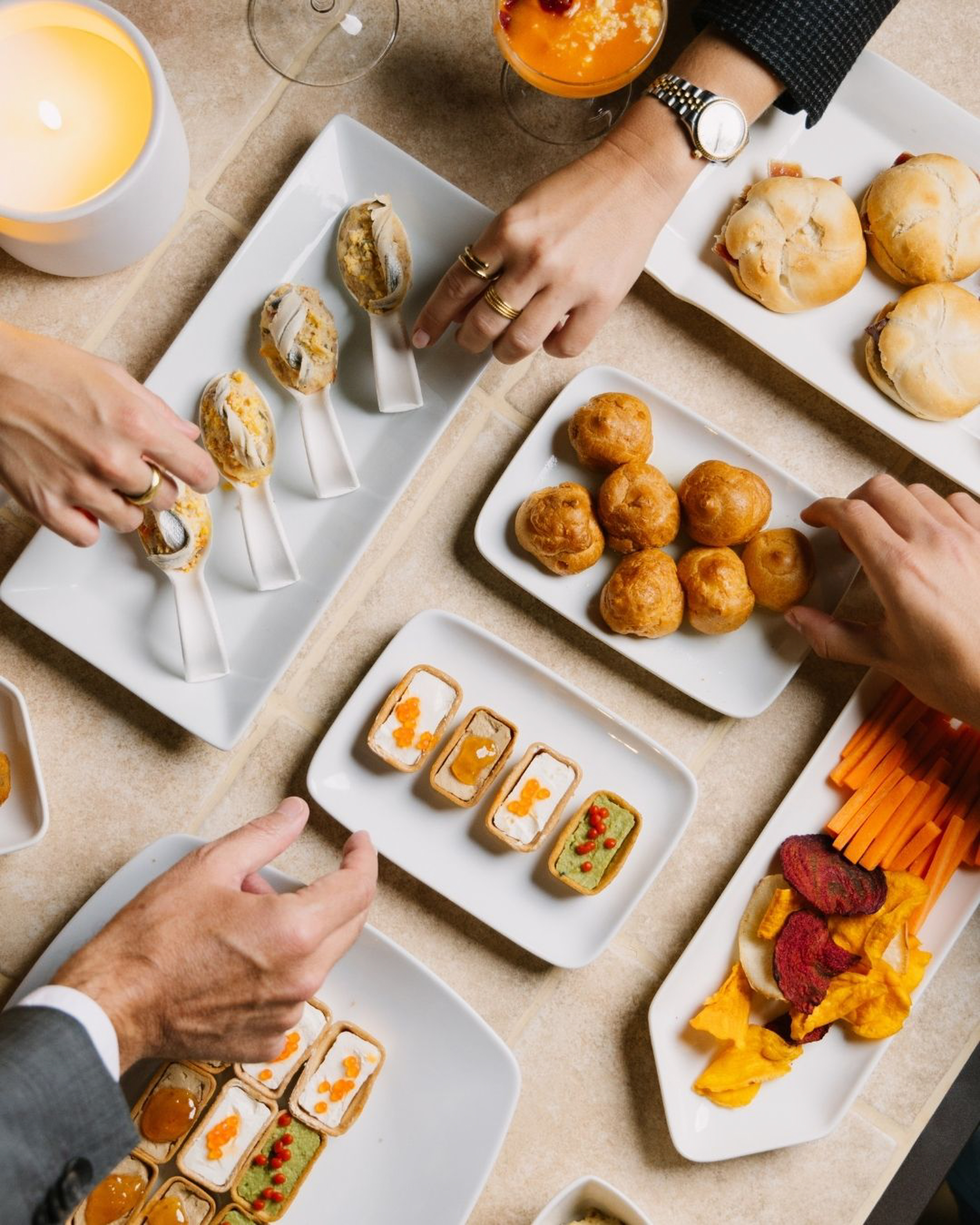 Hands reaching for elegant canapés, mini sandwiches, and gourmet appetizers.