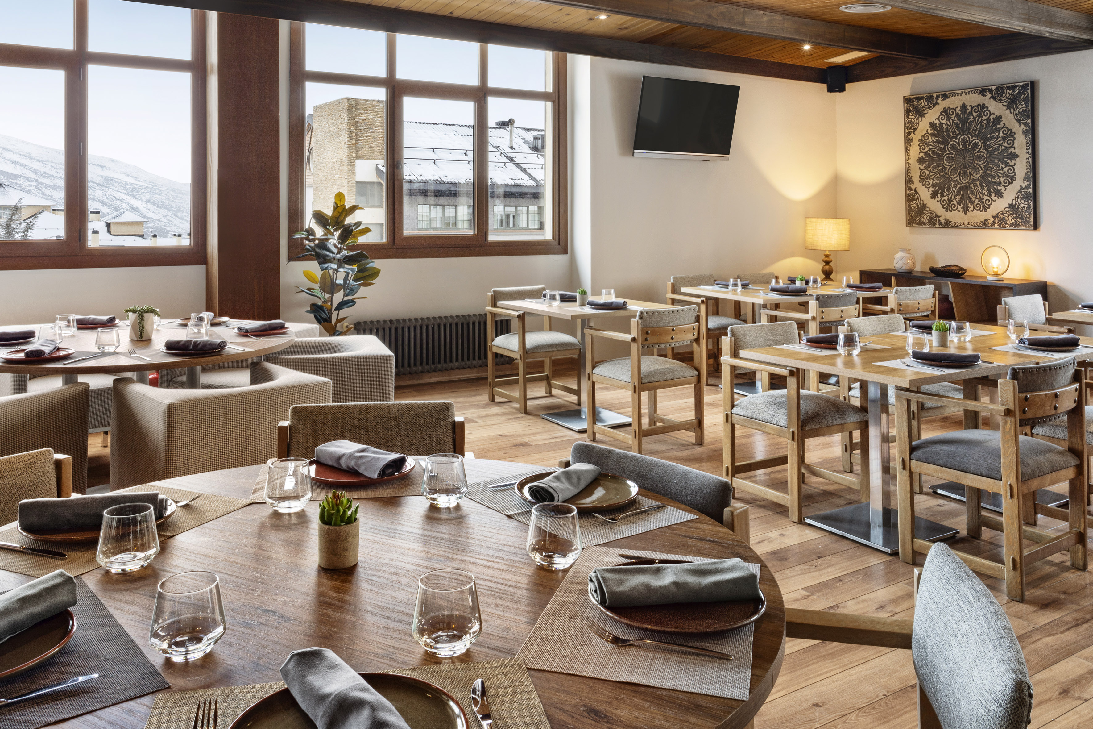 Modern restaurant dining room with wooden tables and snowy mountain window views.