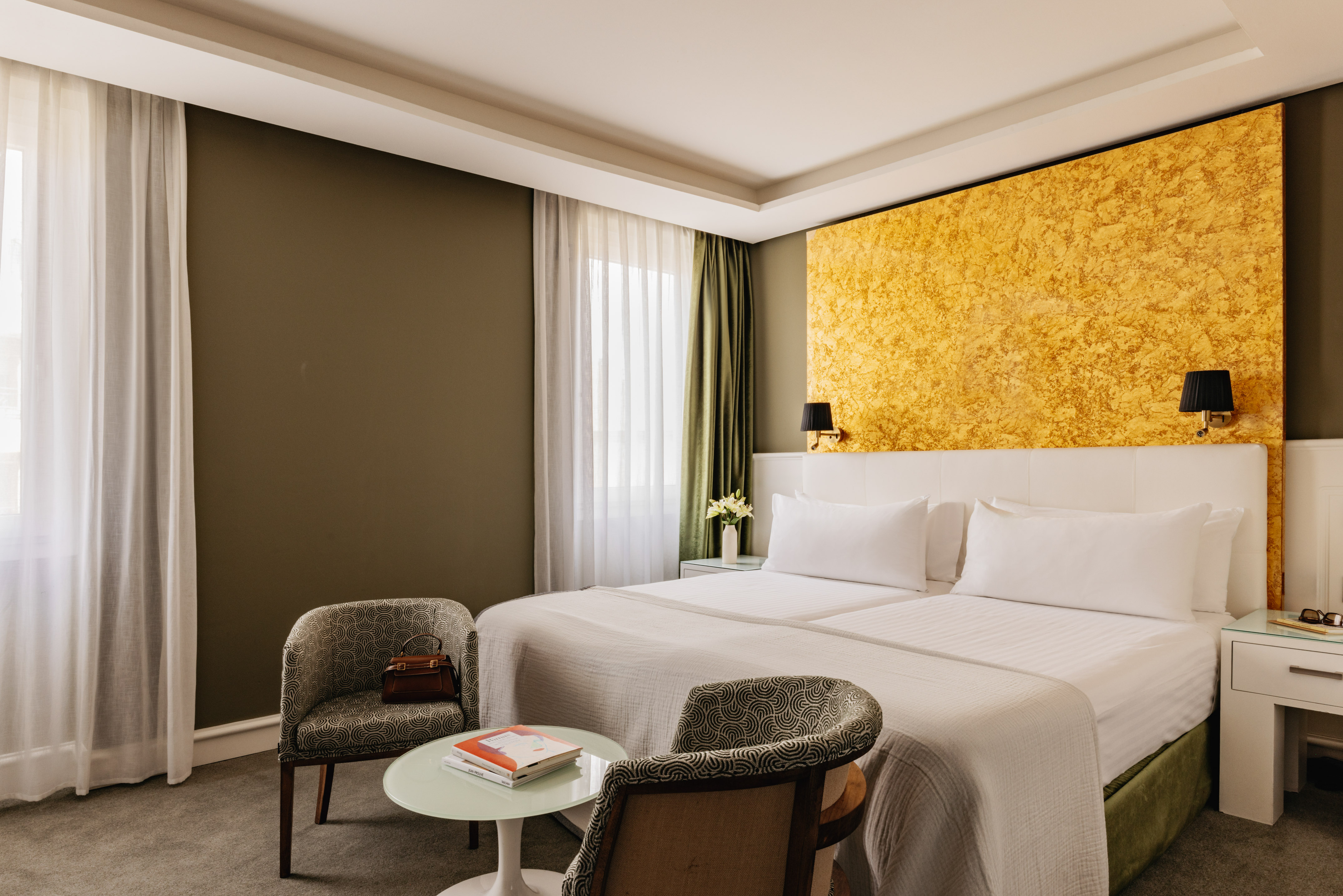 Dormitorio de hotel moderno con dos camas y pared decorativa dorada.