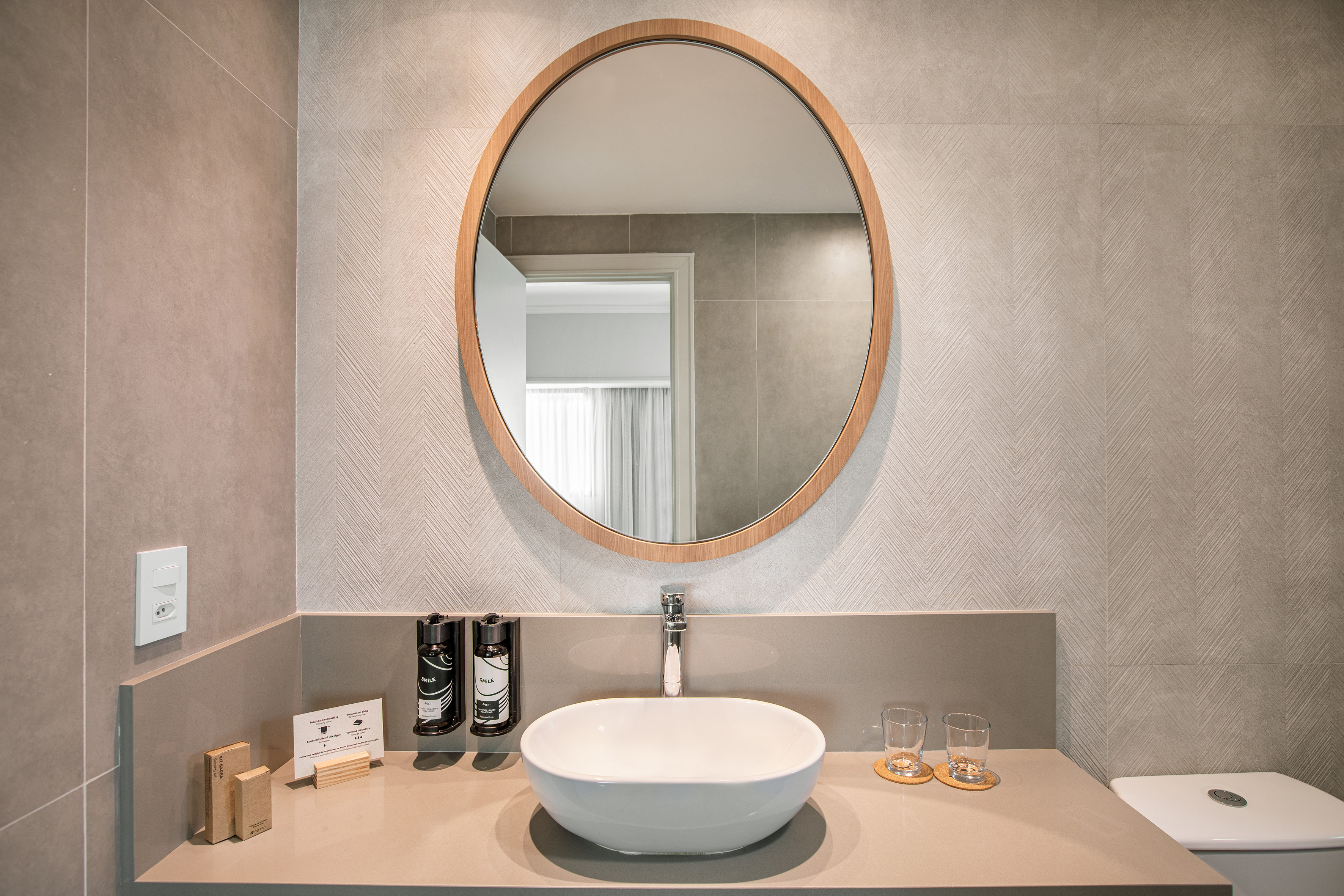 Hotel bathroom with oval wood mirror, vessel sink, and gray patterned walls.