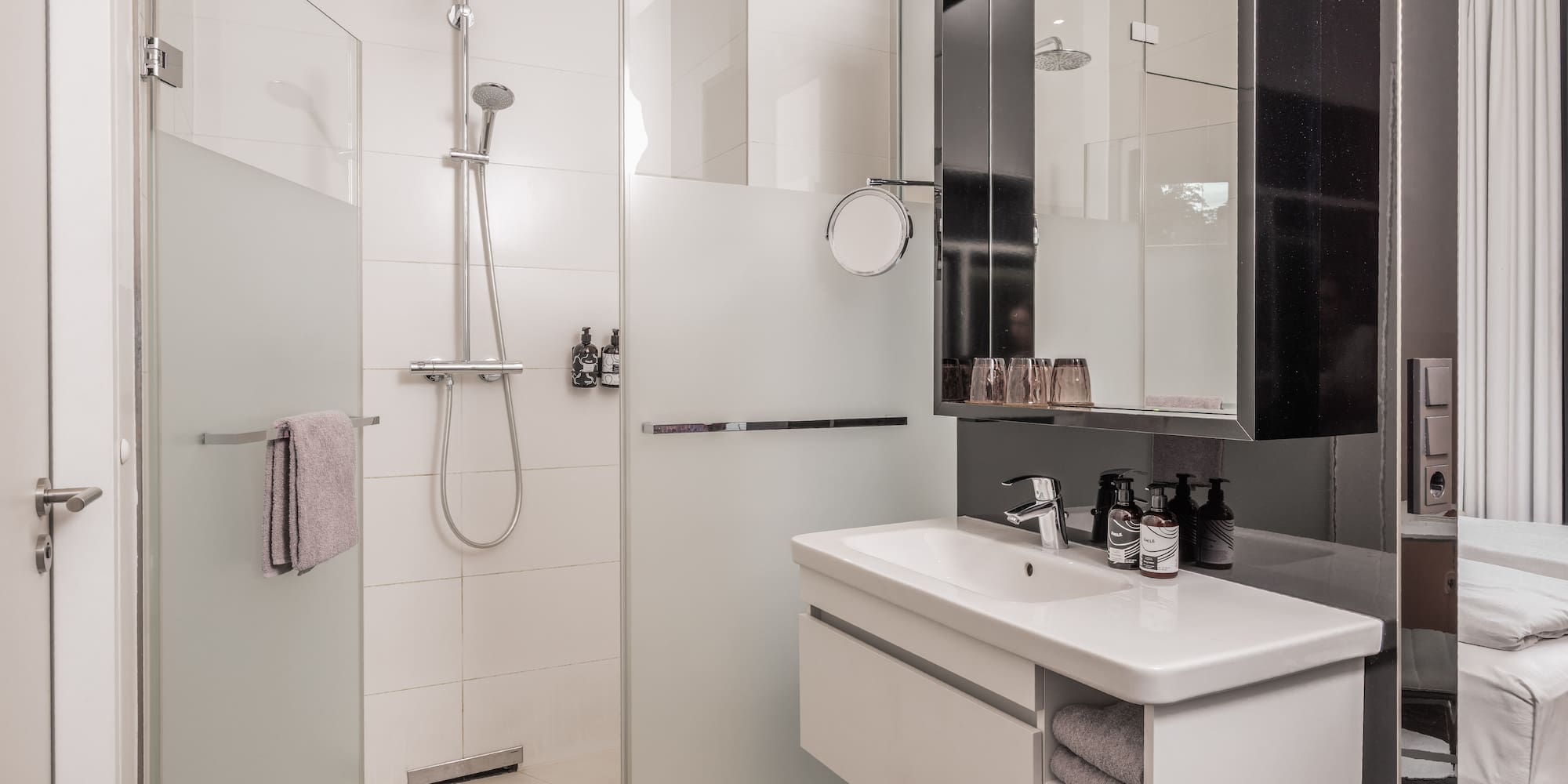 Modern hotel bathroom with walk-in glass shower, white vanity, and mirror.