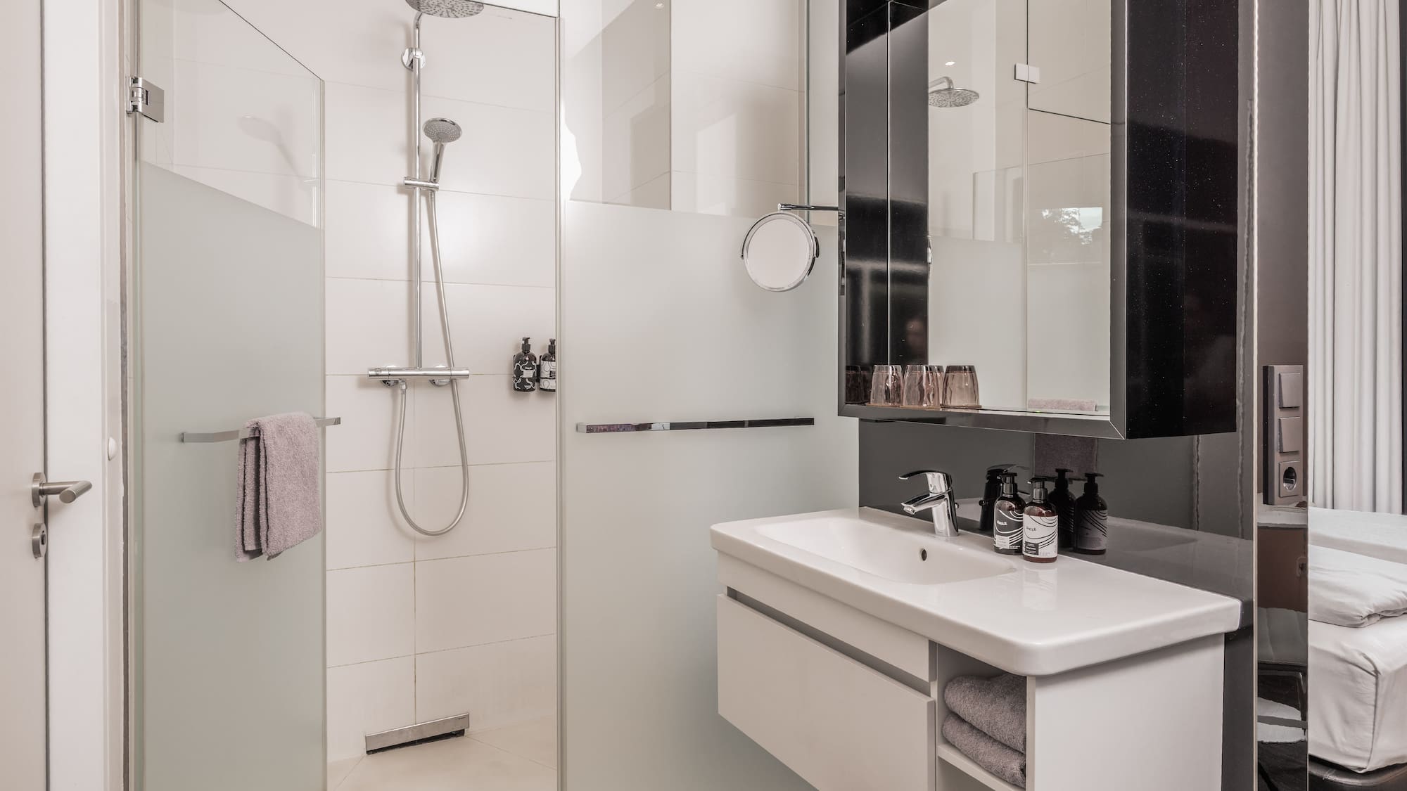 Modern hotel bathroom with walk-in glass shower, white vanity, and mirror.