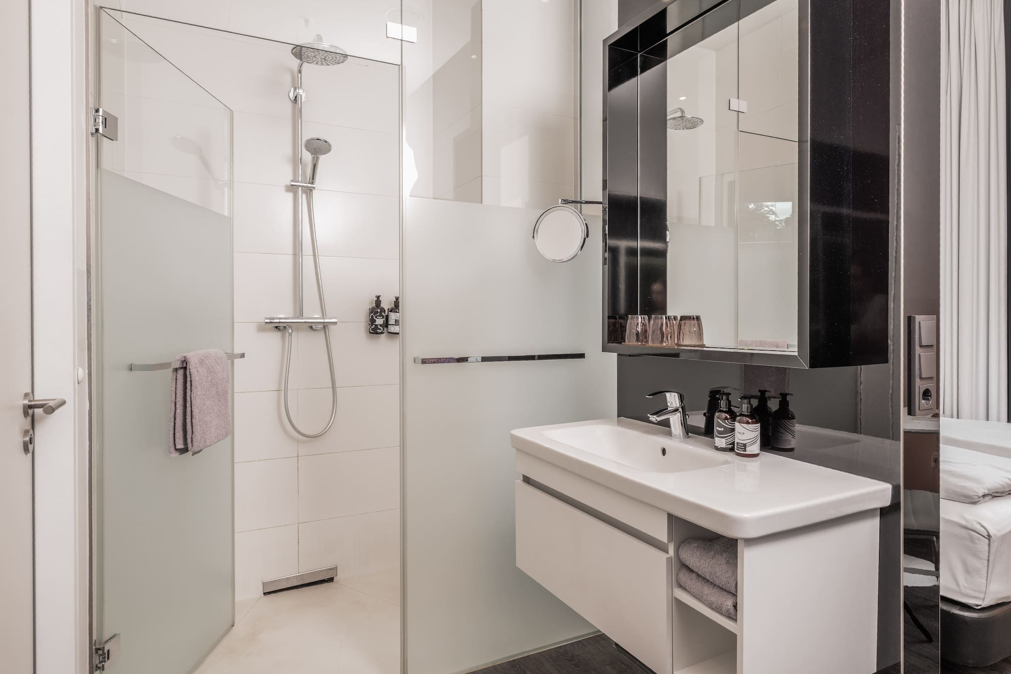 Modern hotel bathroom with walk-in glass shower, white vanity, and mirror.