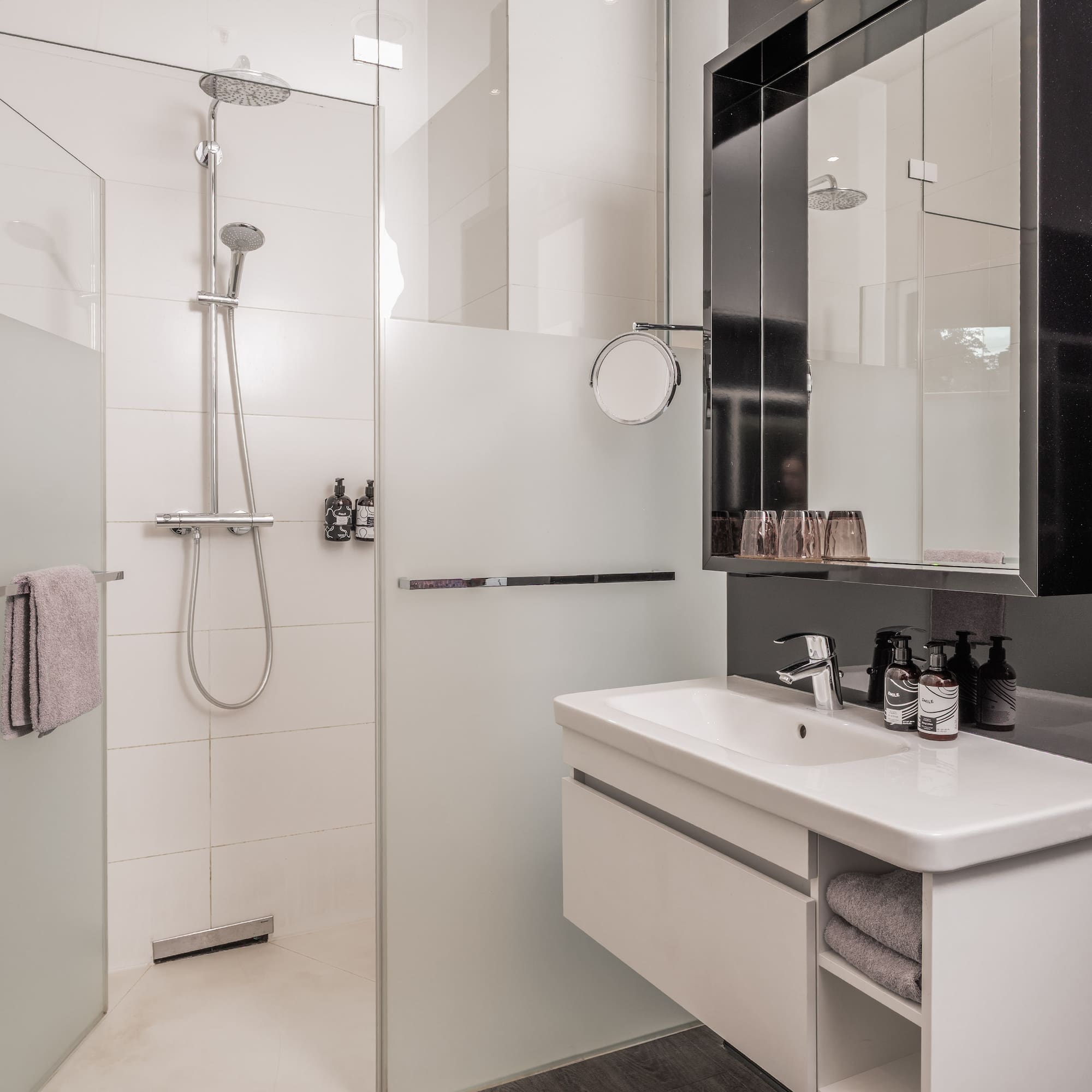 Modern hotel bathroom with walk-in glass shower, white vanity, and mirror.
