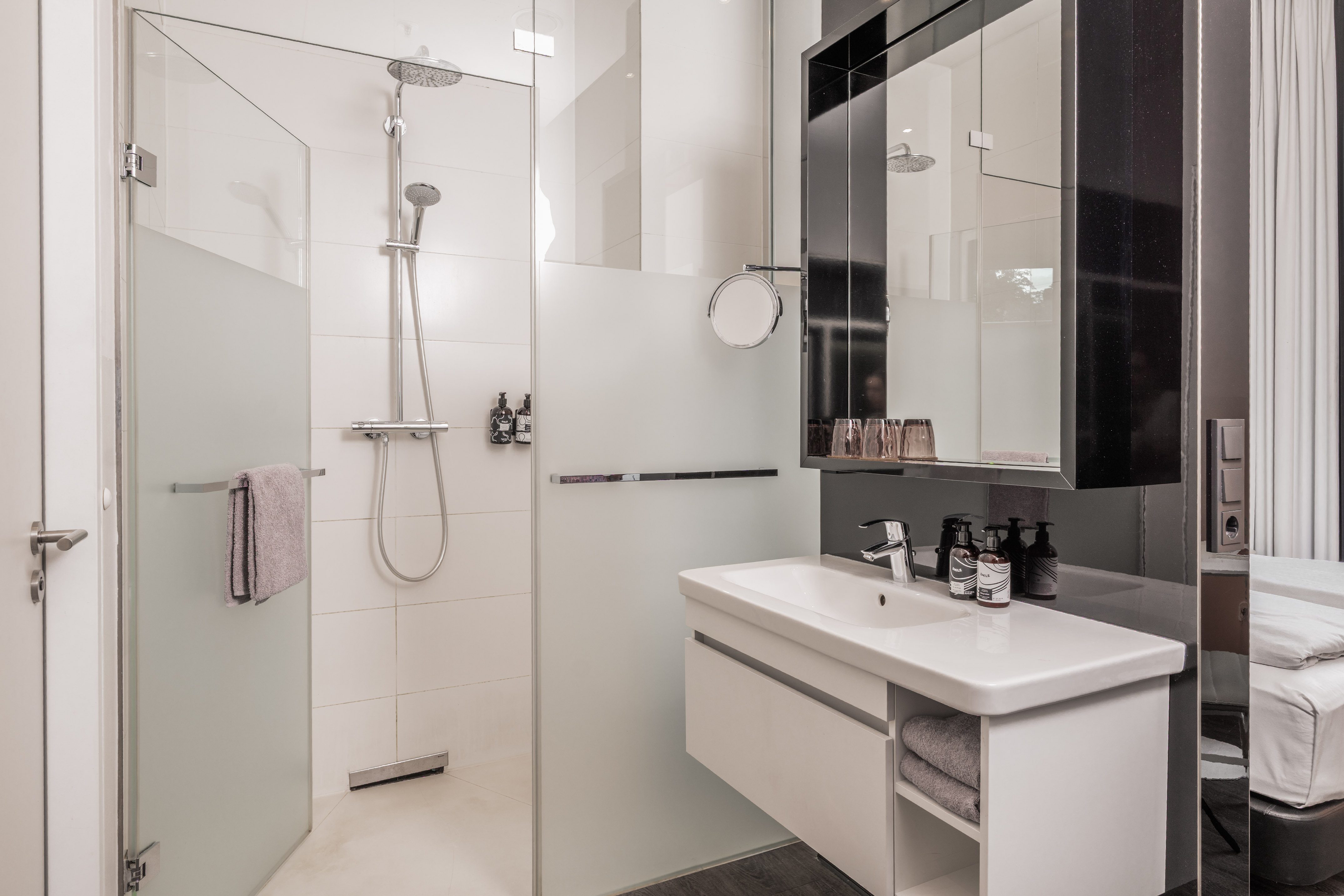 Modern hotel bathroom with walk-in glass shower, white vanity, and mirror.