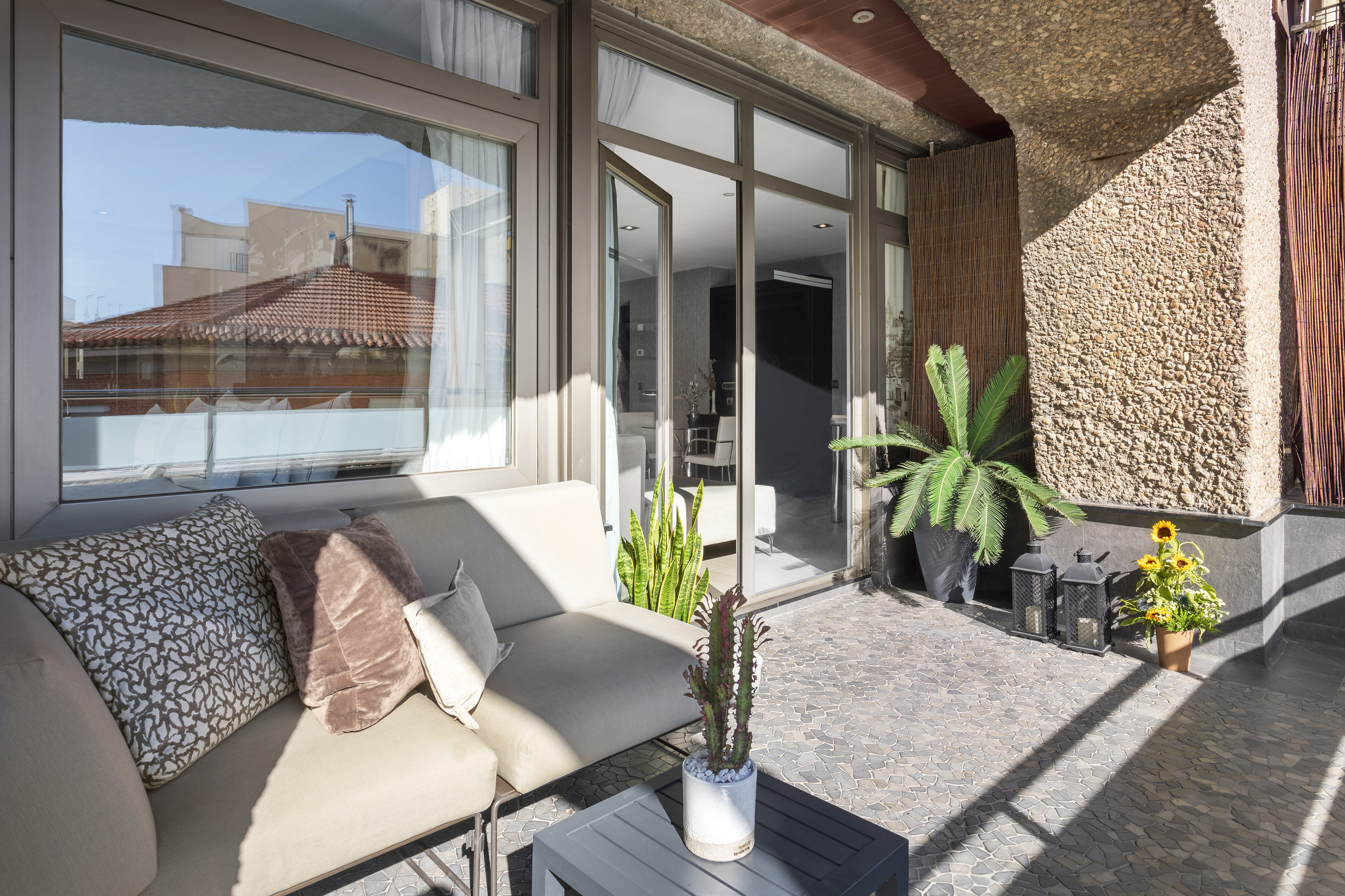 Apartment balcony with sofa, potted plants, glass doors, and stone flooring.