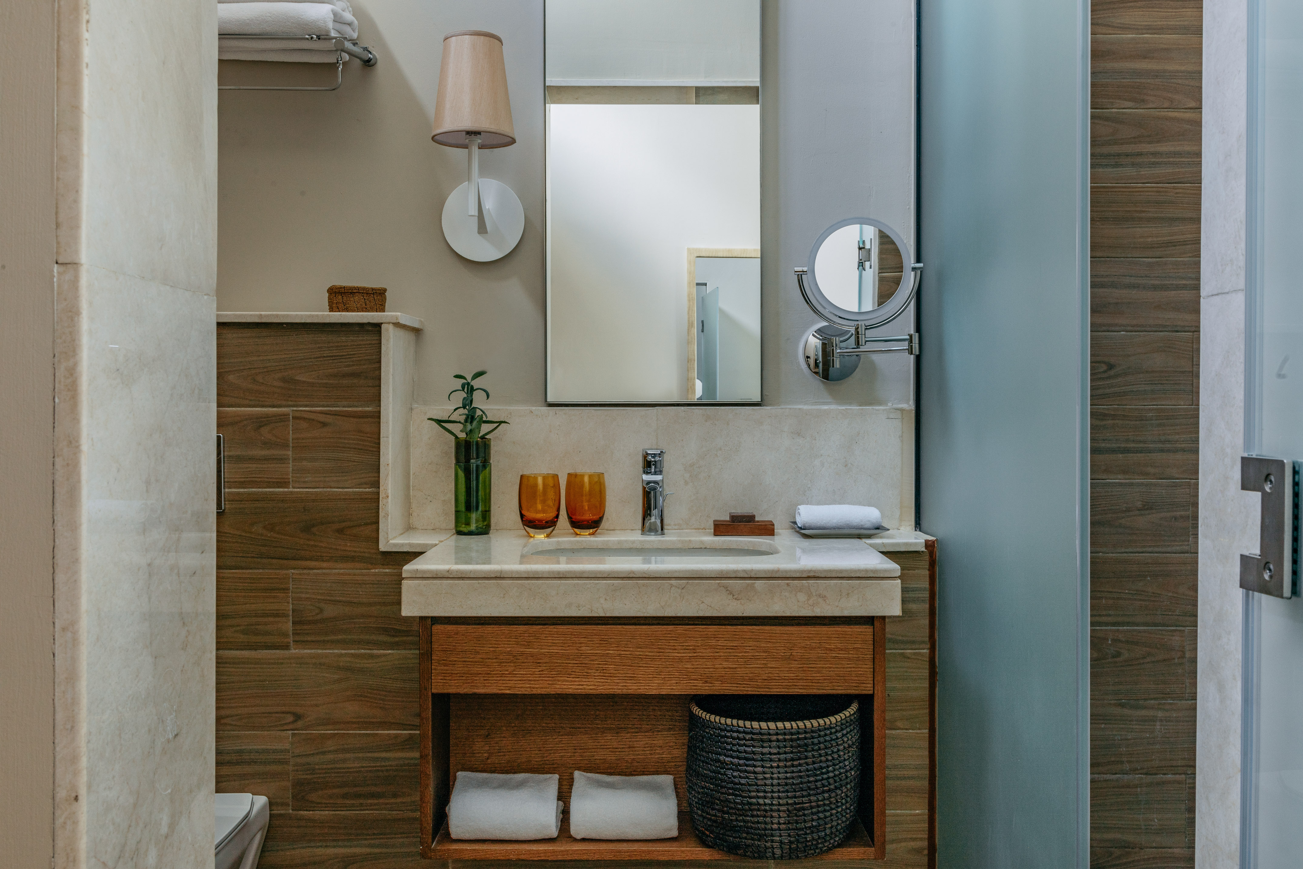 Modern bathroom vanity with marble countertop, wood cabinet, mirror, and plant.